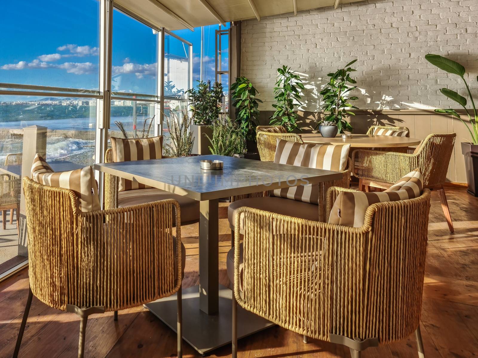 Day sunny view of no people space with chairs & ashtrays on tables with a glass panel before the seafront in Thessaloniki, Greece.