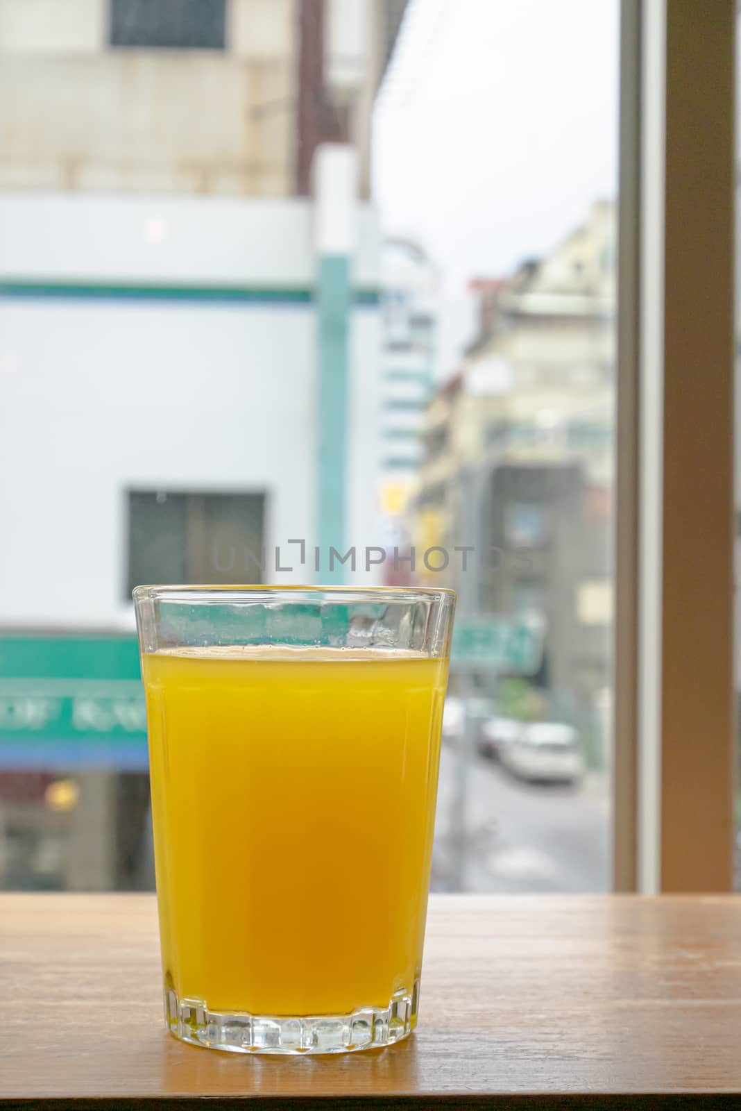 A glass of fresh orange juice drink on brown table with downtown window view background.