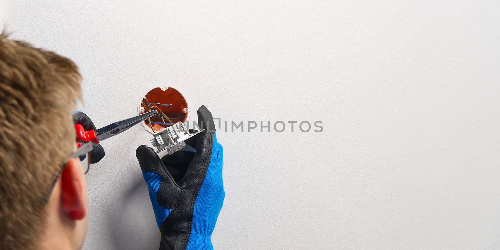 electrician installing light switch on painted wall with screwdriver. Man installing light switch after home renovation. by PhotoTime