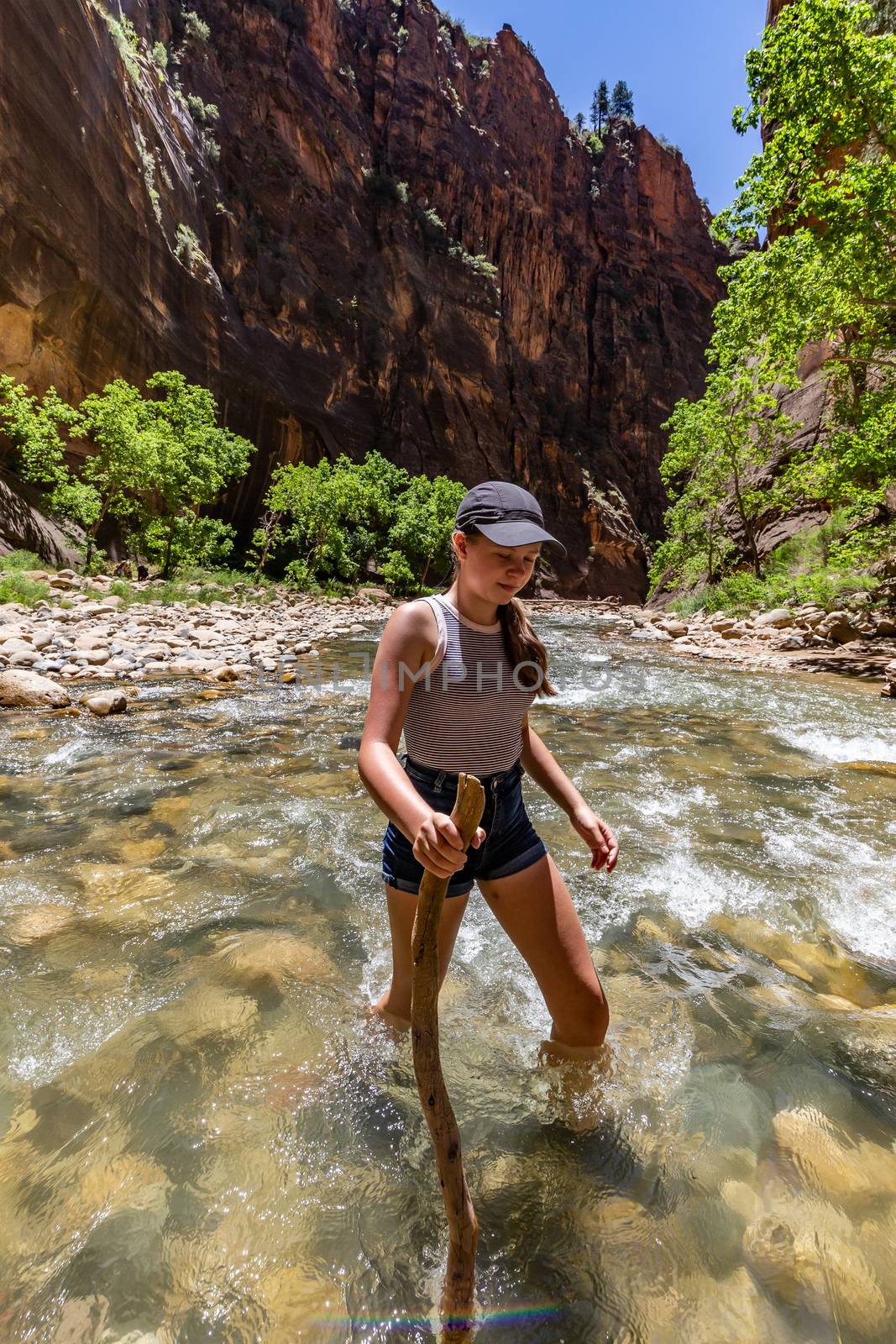Teenage girl holding a stick is crossing the river in Zion Natio by mkenwoo