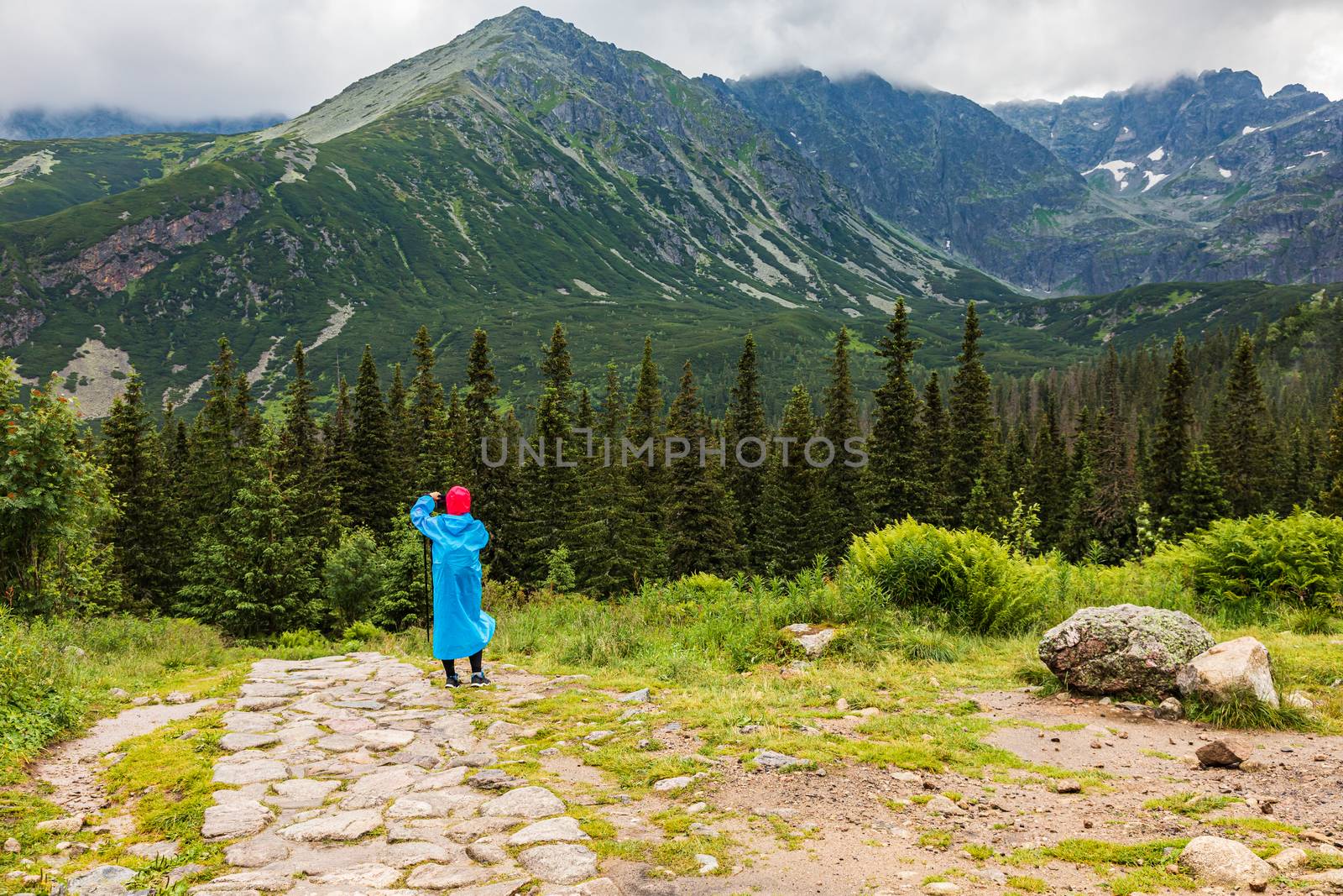 Hikker in a blue plastic raincoat taking picture in Tatra mountains, Poland in bad weather