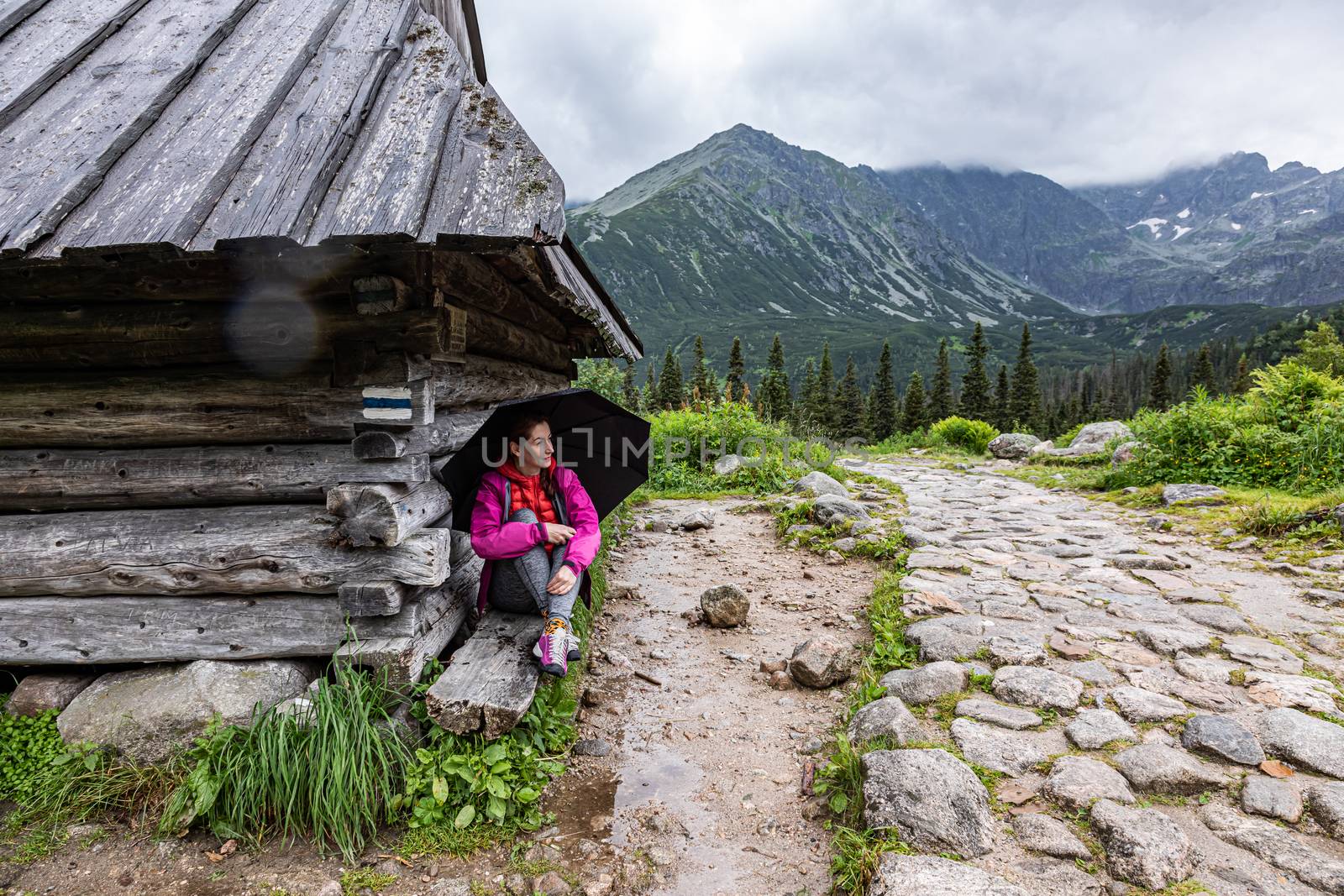 woman hiding from rain under a roof of mountain shelter in Tatra by mkenwoo