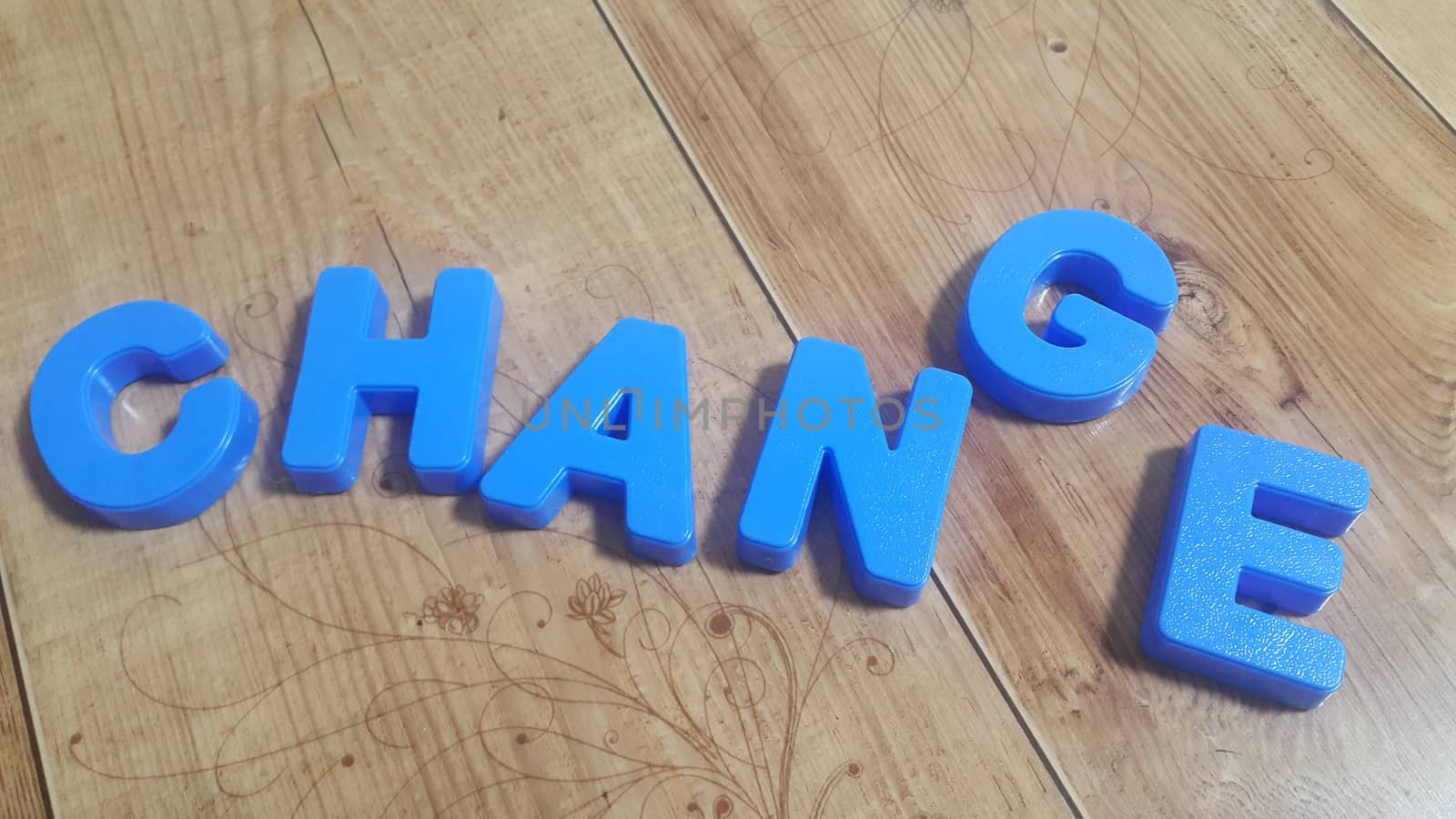 Plastic colored alphabets making words are placed on a wooden floor by Photochowk