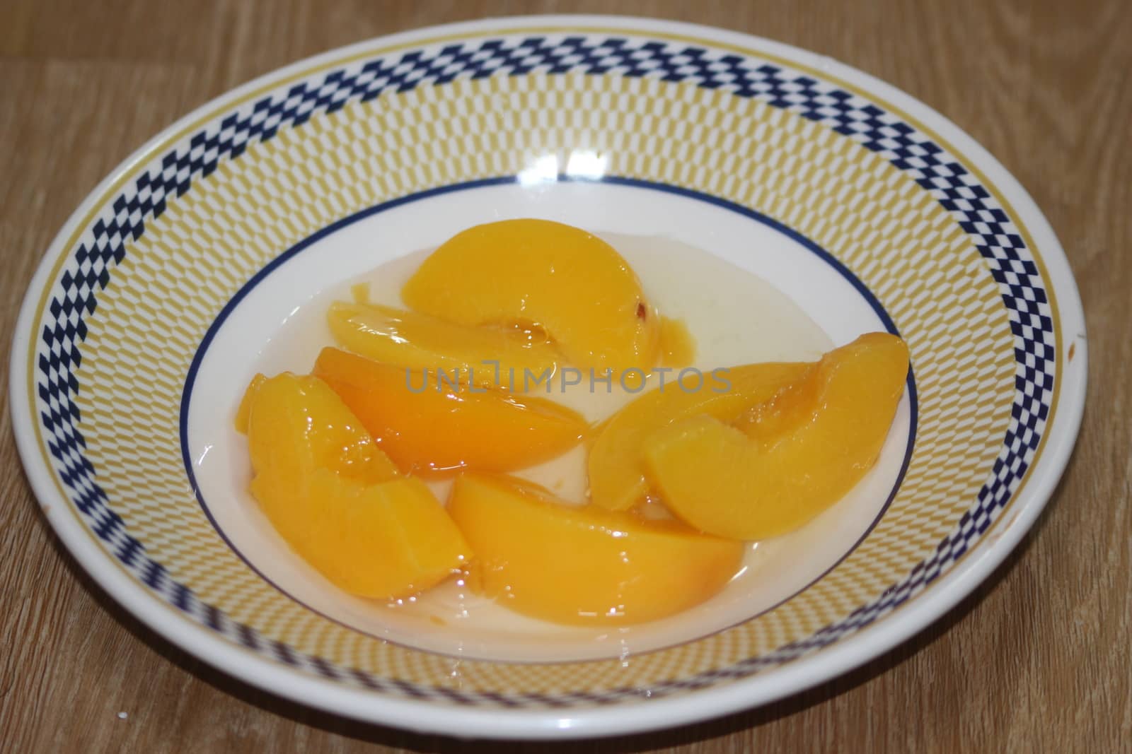 Closeup high angle view with selective focus of yellow peaches slices. Canned peaches halves sprinkled with syrup in white plate.