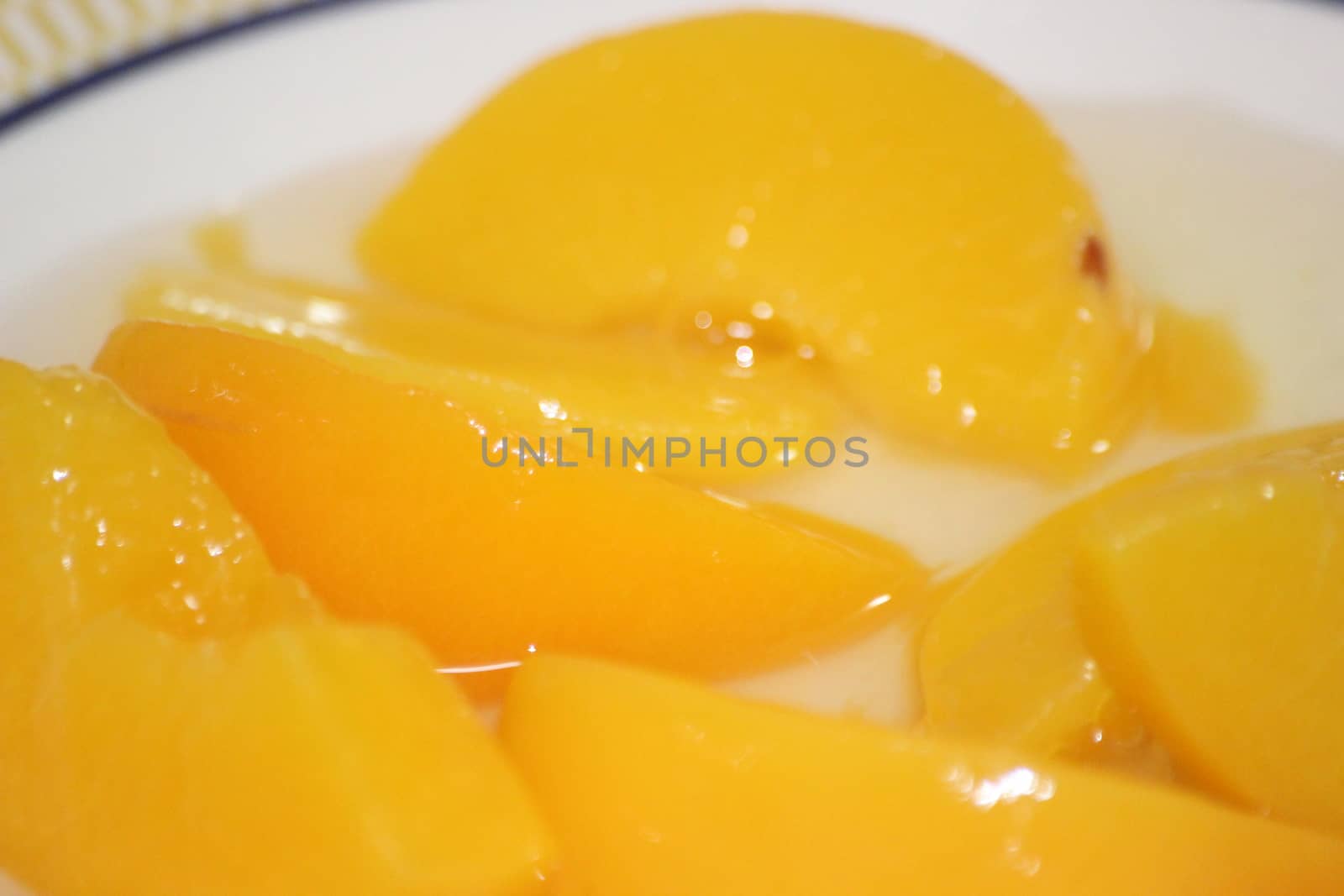 Closeup high angle view with selective focus of yellow peaches slices. Canned peaches halves sprinkled with syrup in white plate.