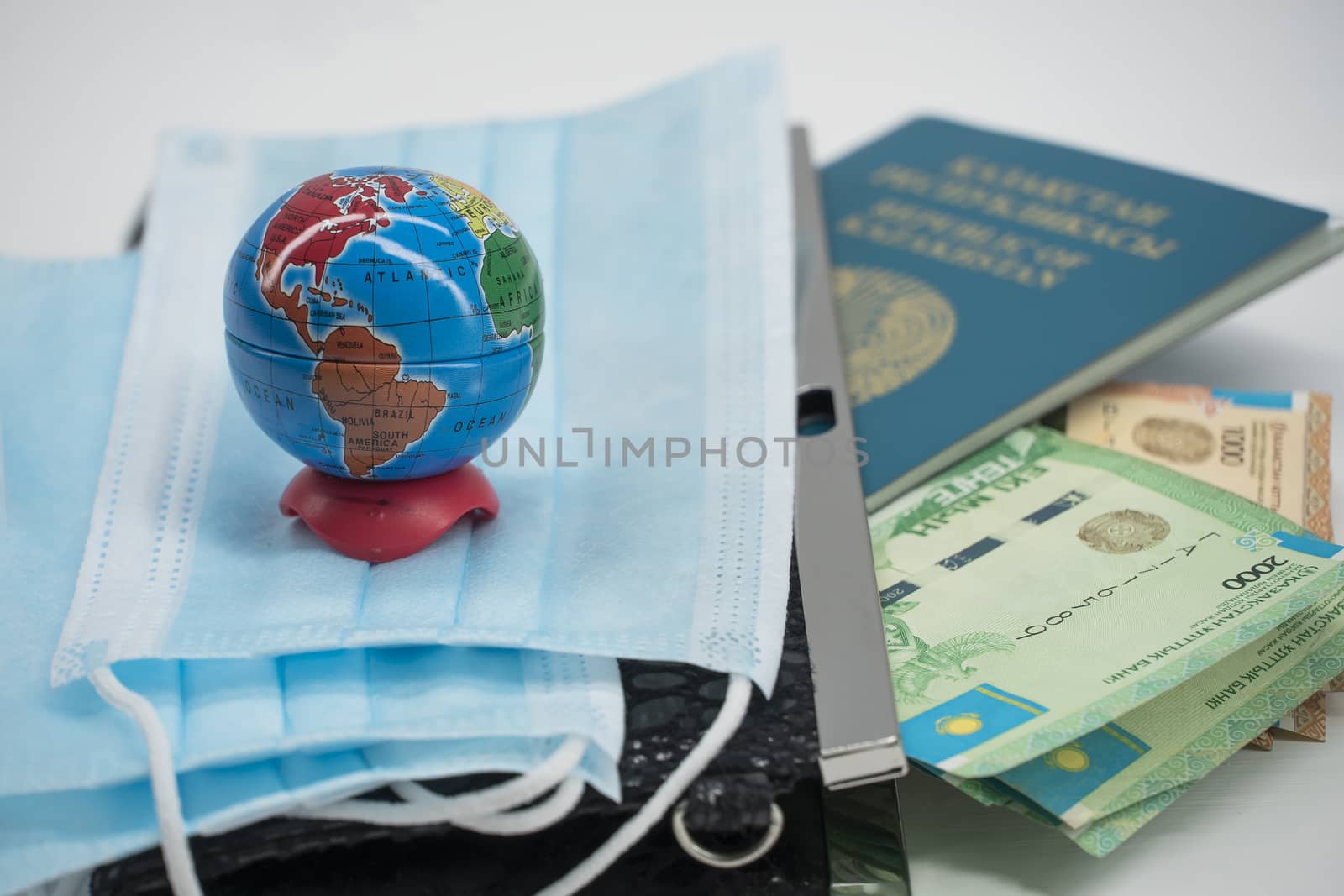 Quarantine in Kazakhstan. Tenge money with medical face masks, a globe, a card and a passport are on the table. The closure of borders and travel in Kazakhstan.