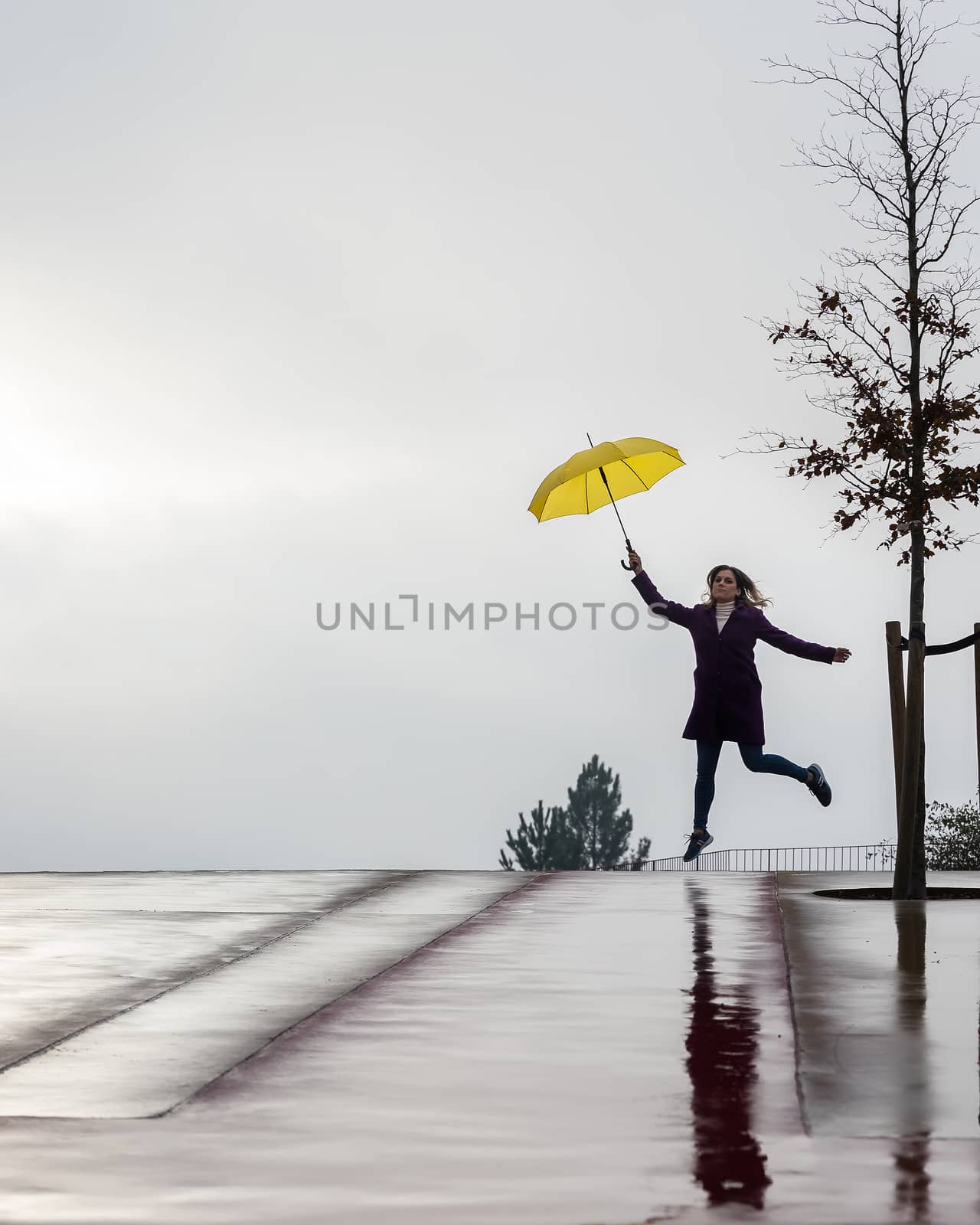 Woman jumping on the horizon with a yellow umbrella on a rainy day. Space for your text.