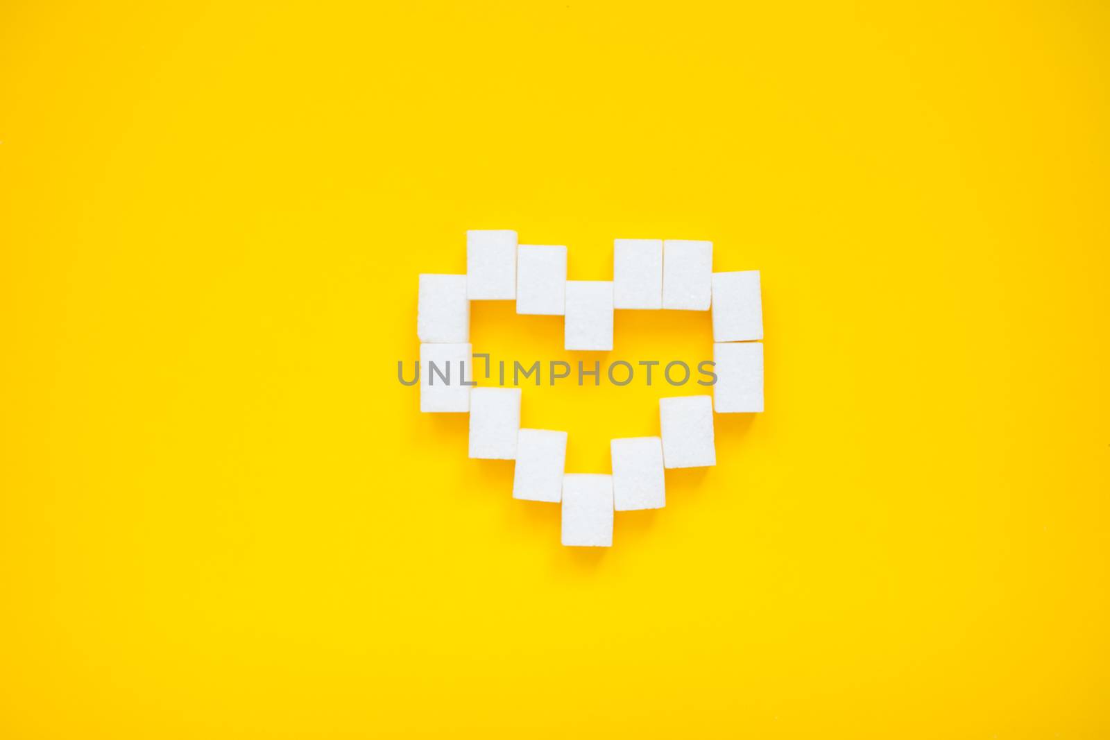 Heart made of pressed sugar cubes on a yellow background. Diabetes.