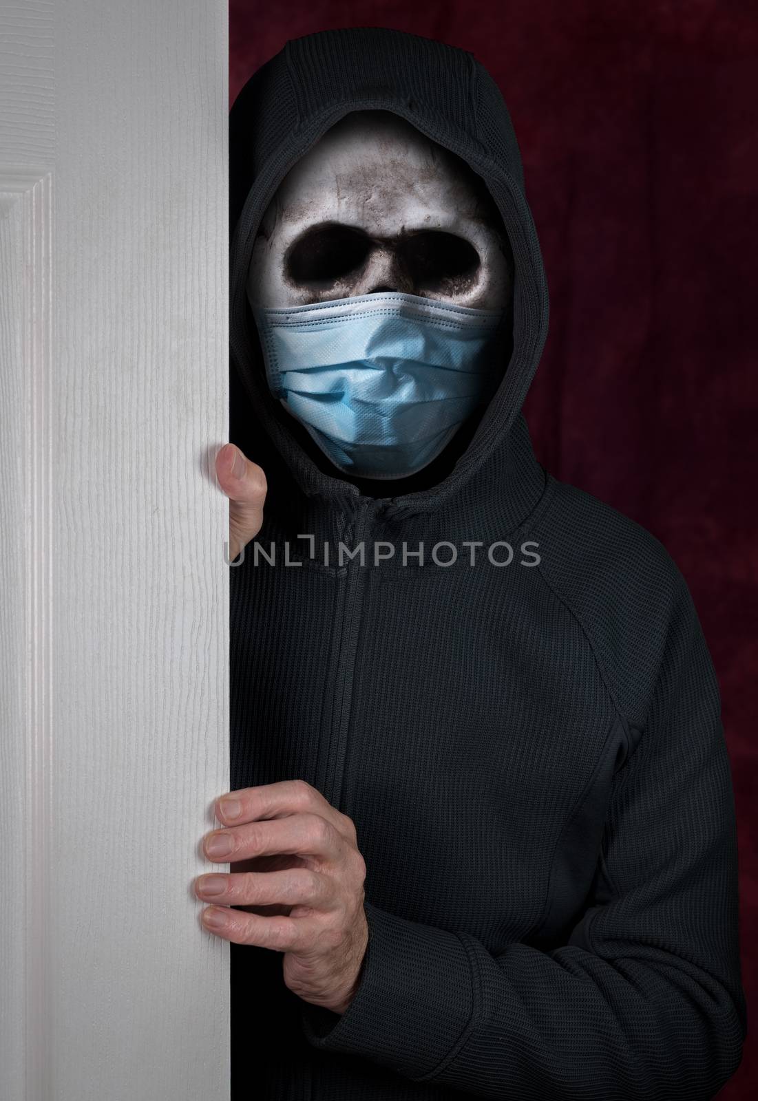 Halloween theme of stalker with skull and face mask against coronavirus entering a home by steheap