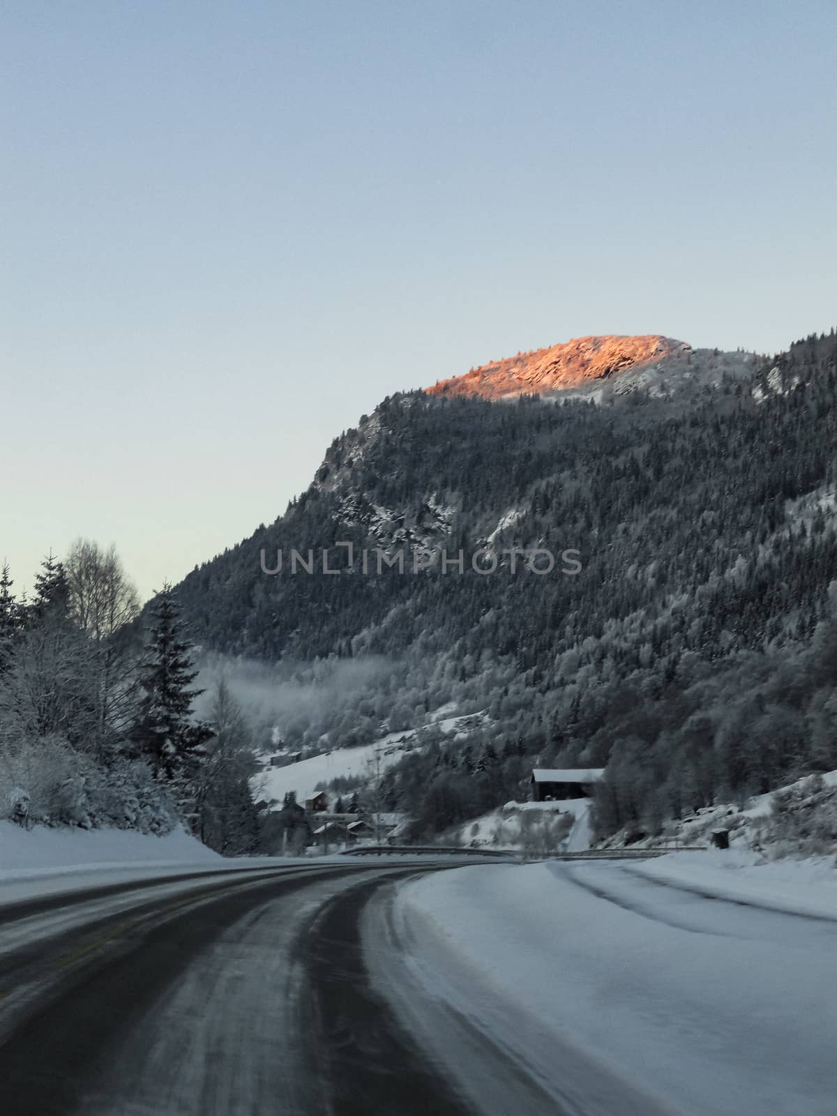 Driving at sunrise through mountains and forests in Norway. by Arkadij