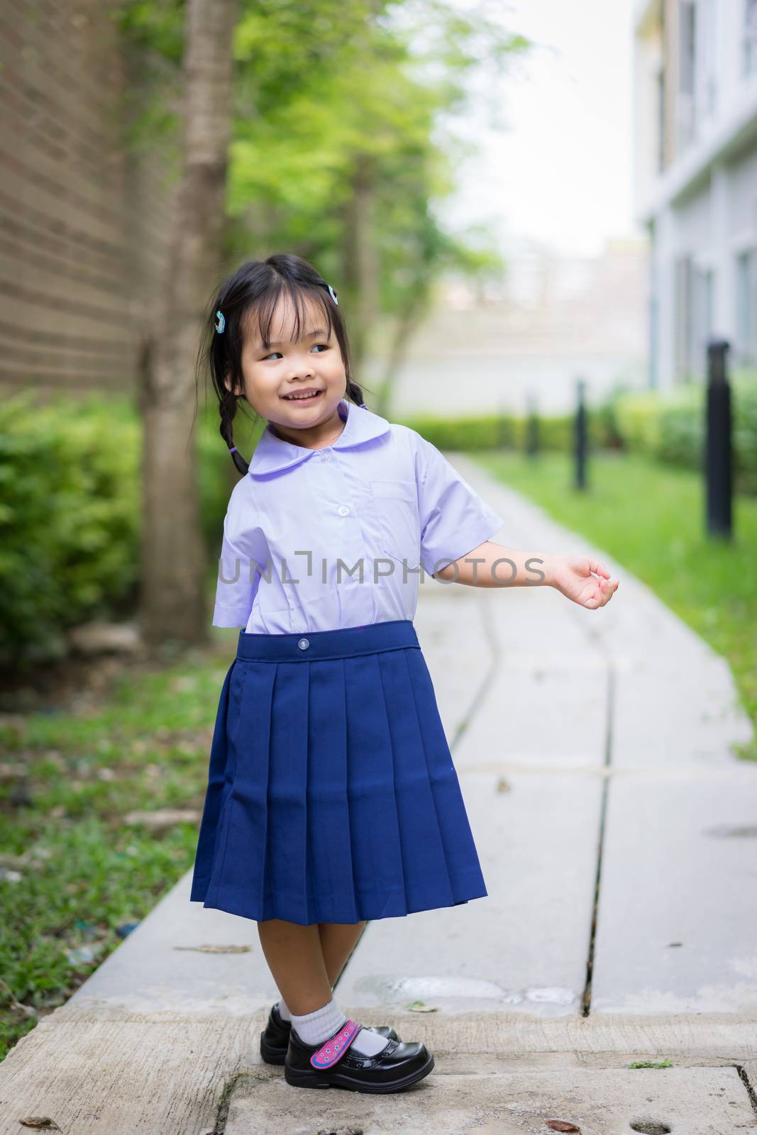 Portrait of happy little girl in Thai school uniform standing in by domonite