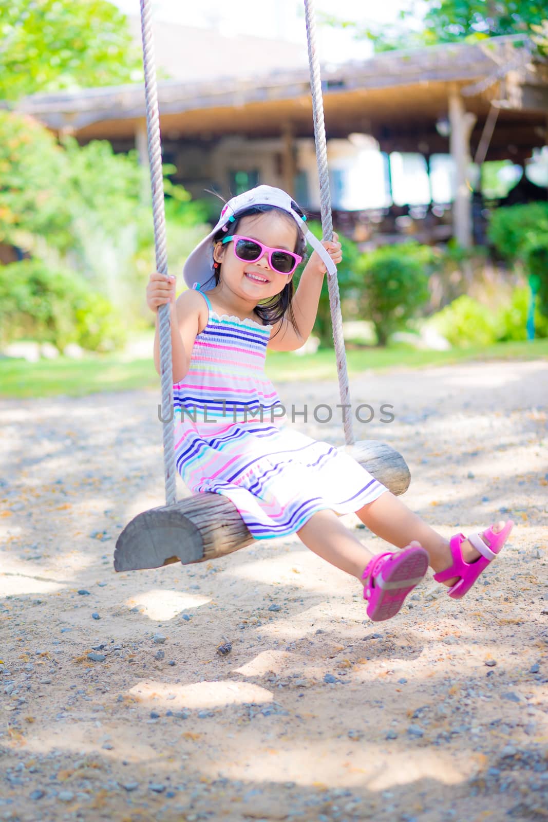 Little girl wear sunglasses sitting on a swing in the park by domonite