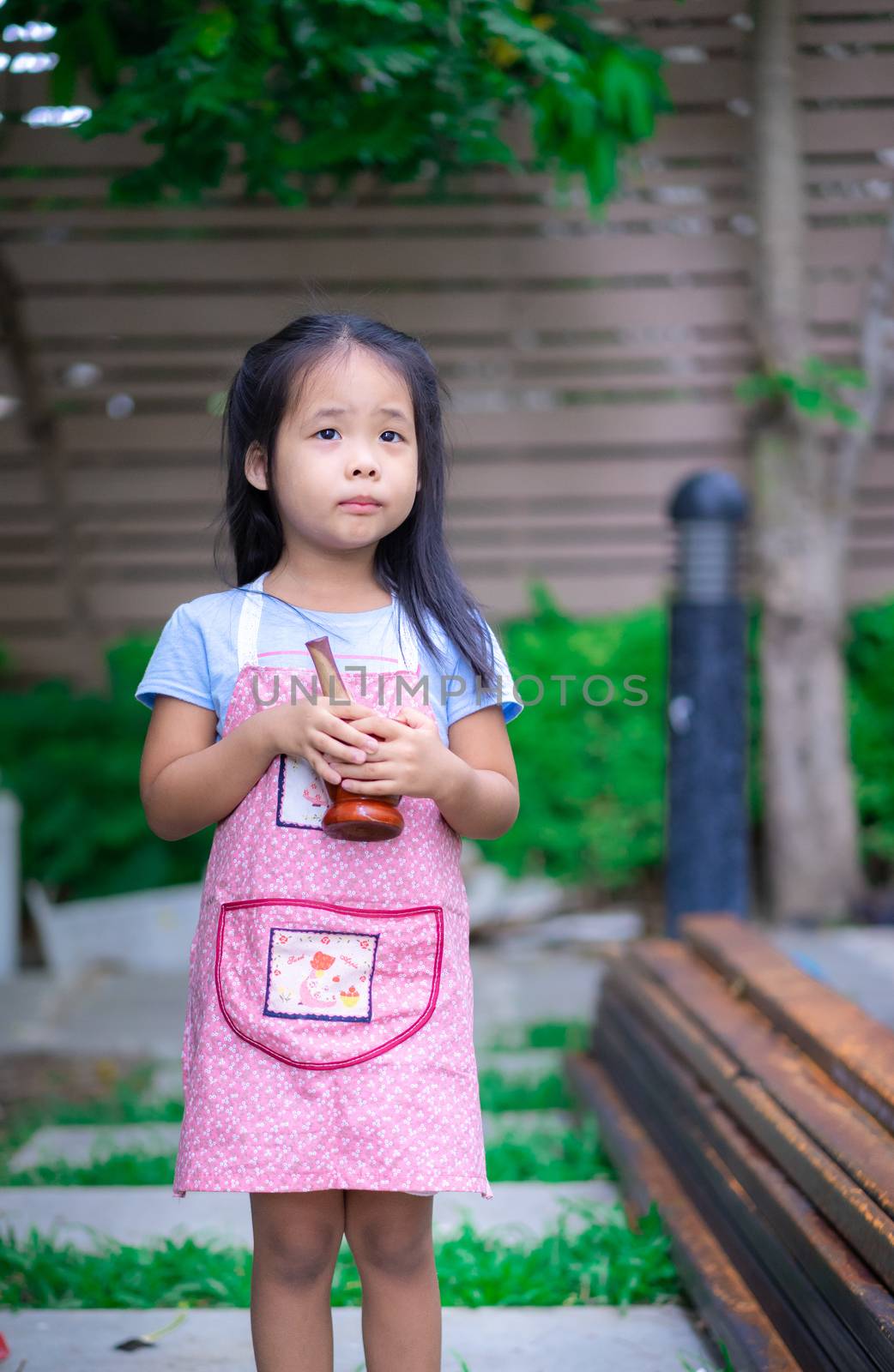 Portrait of little girl in apron with mortar in the garden