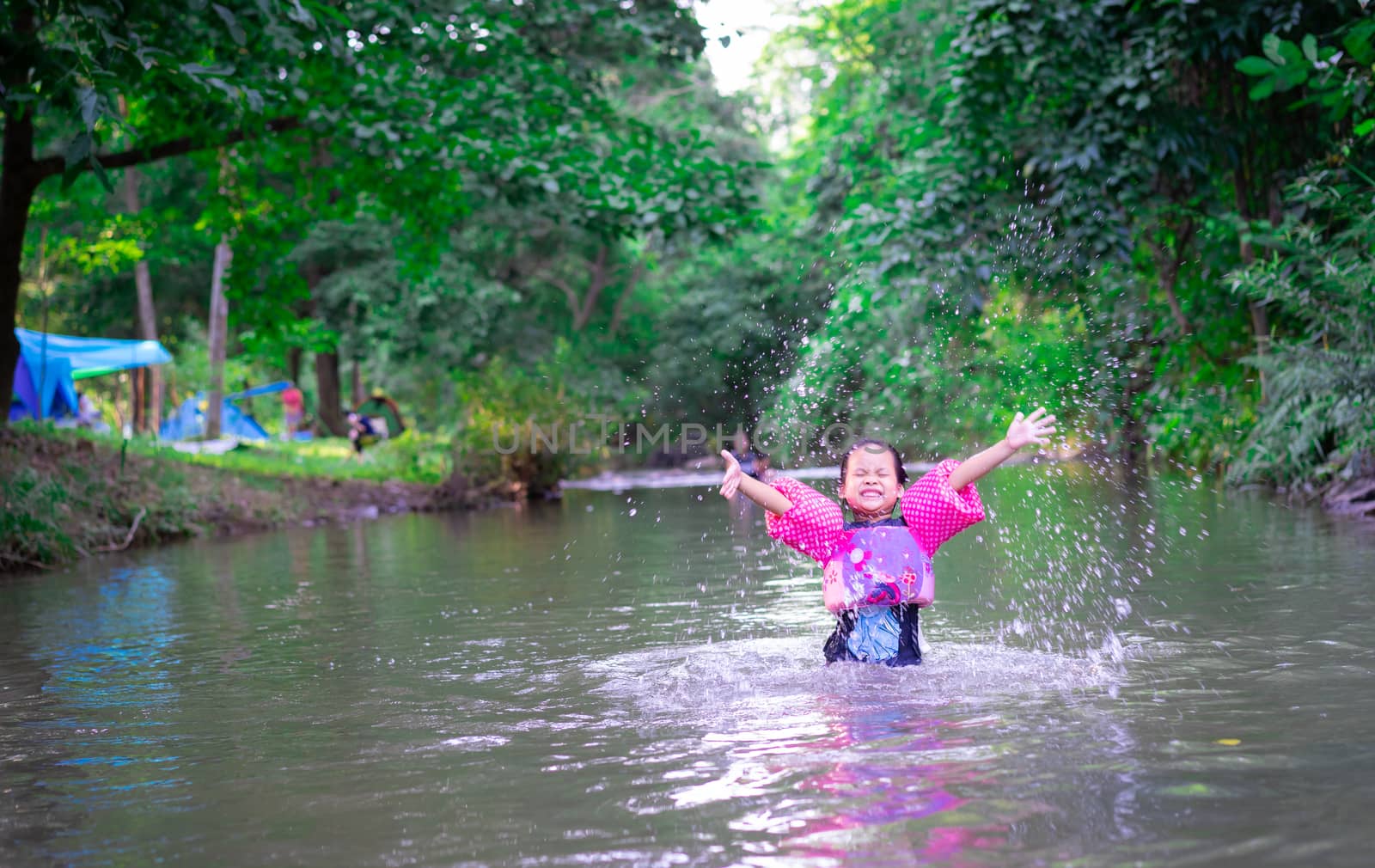 little asian girl wearing inflatable sleeves playing in nature water while camping on holiday