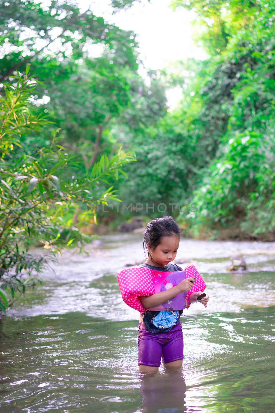 little asian girl wearing inflatable sleeves playing in nature water on holiday