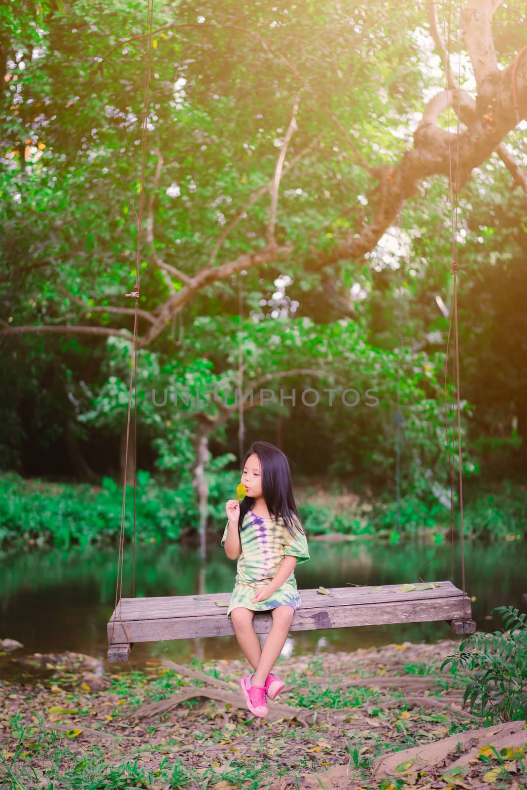 Little girl in green dress sitting on a swing in the park by domonite
