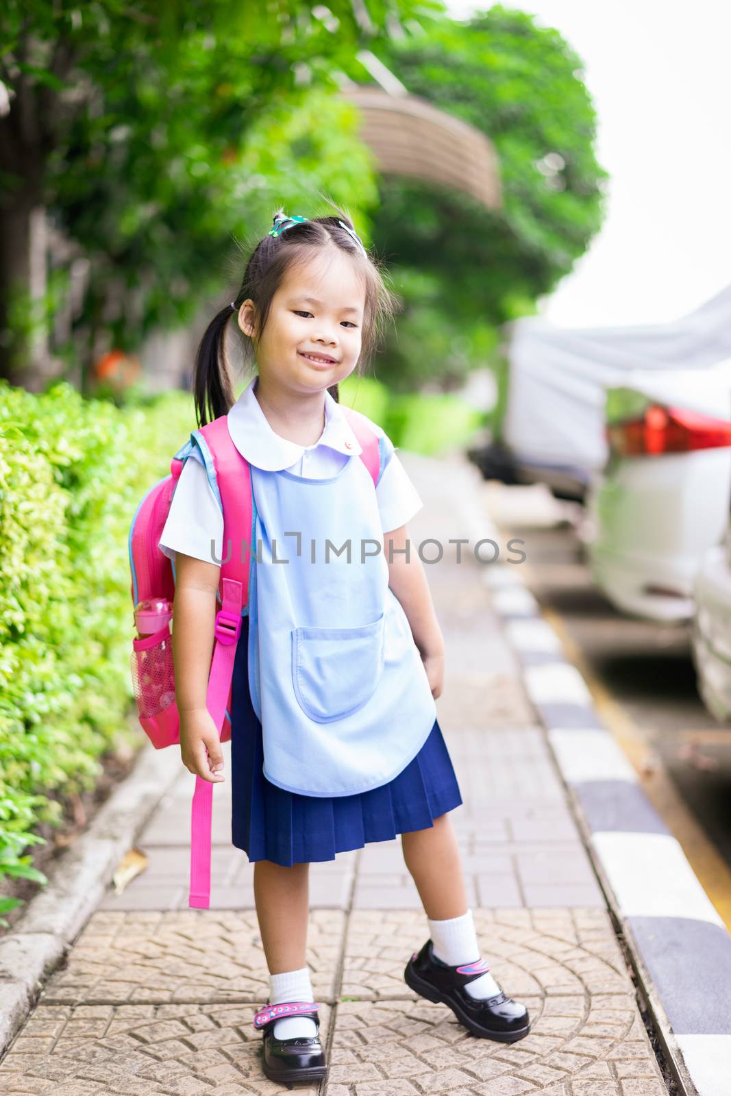 Portrait of happy little girl in Thai school uniform with backpack standing footpath, ready back to school