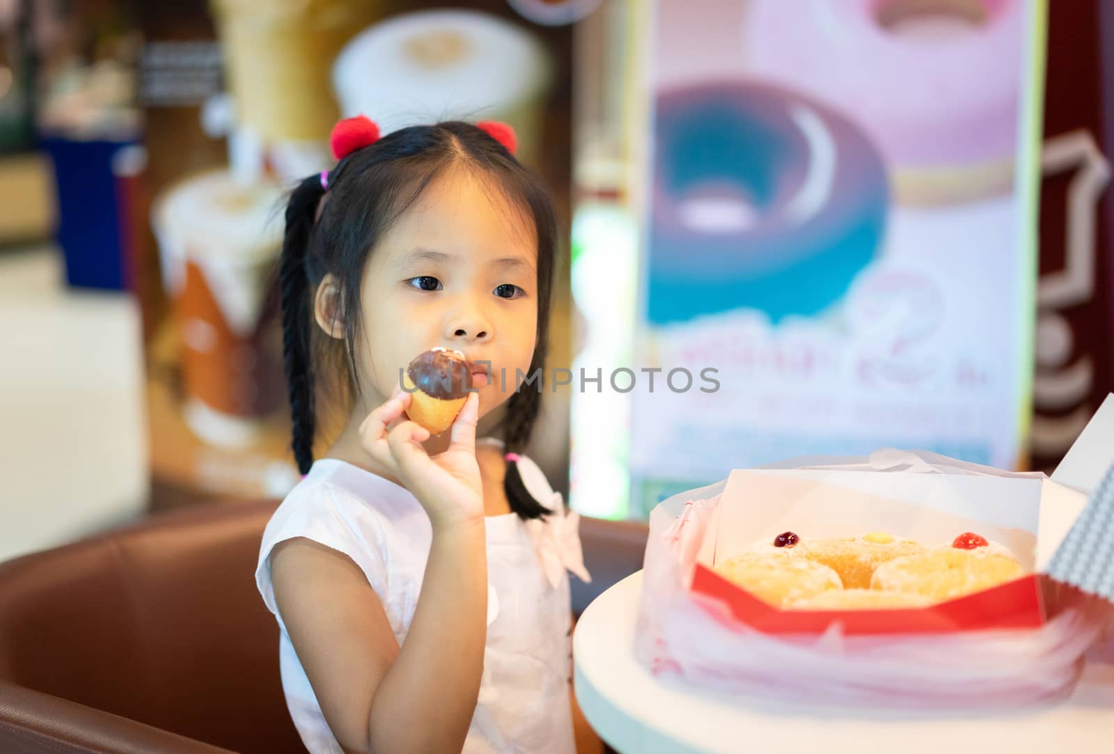 Little asian girl sitting on the chair with holding and eating donuts
