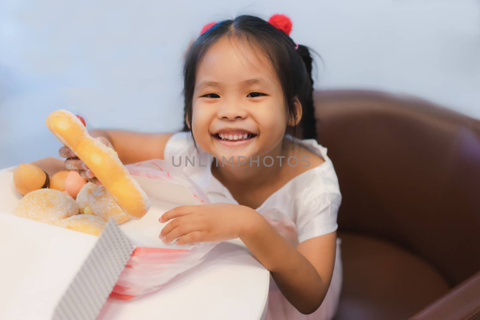 Little asian girl sitting on the chair with holding and eating donuts