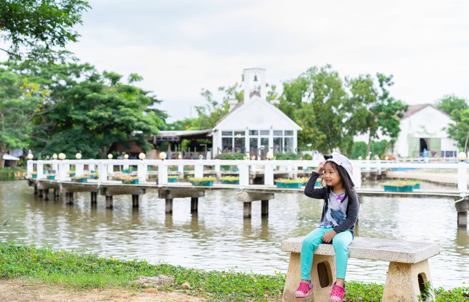 little girl wear hat sitting on a bench near the pond