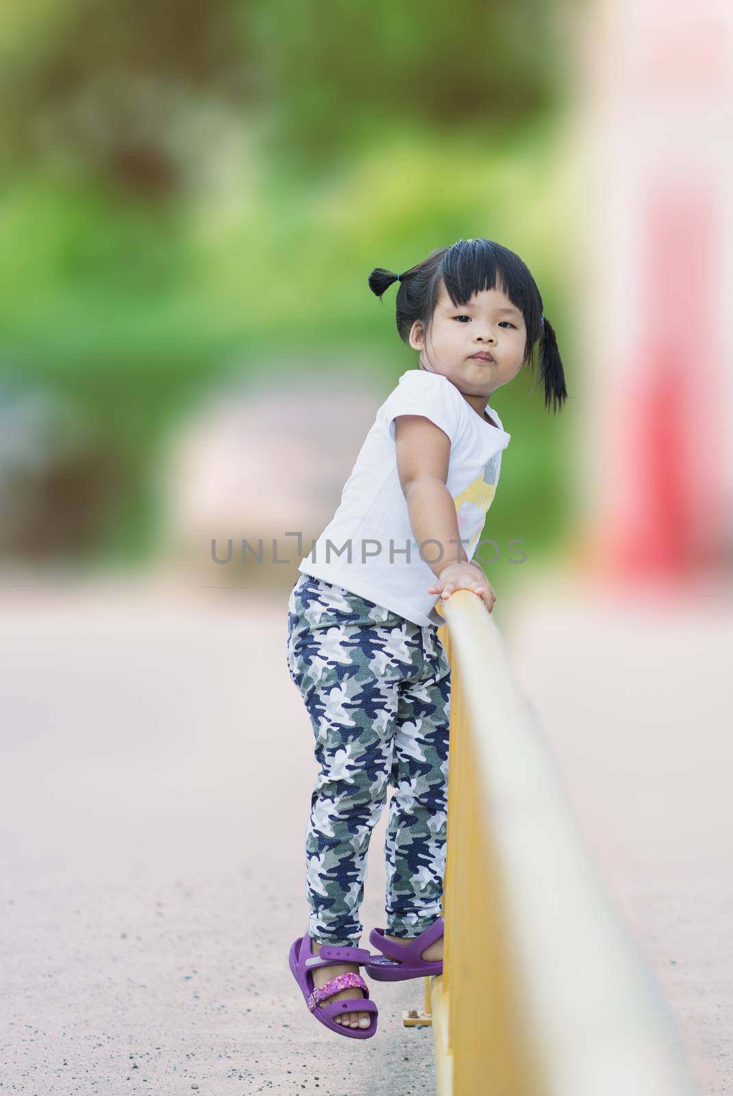 Girl climbing yellow fencein the park