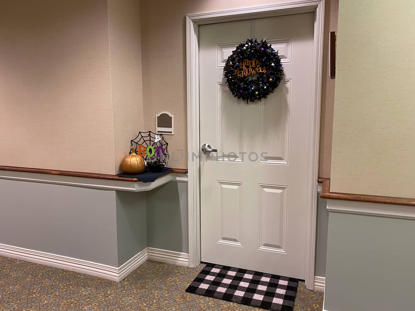 A residents door at a senior living facility decorated with a wreath, pumpkin and spider web for halloween,