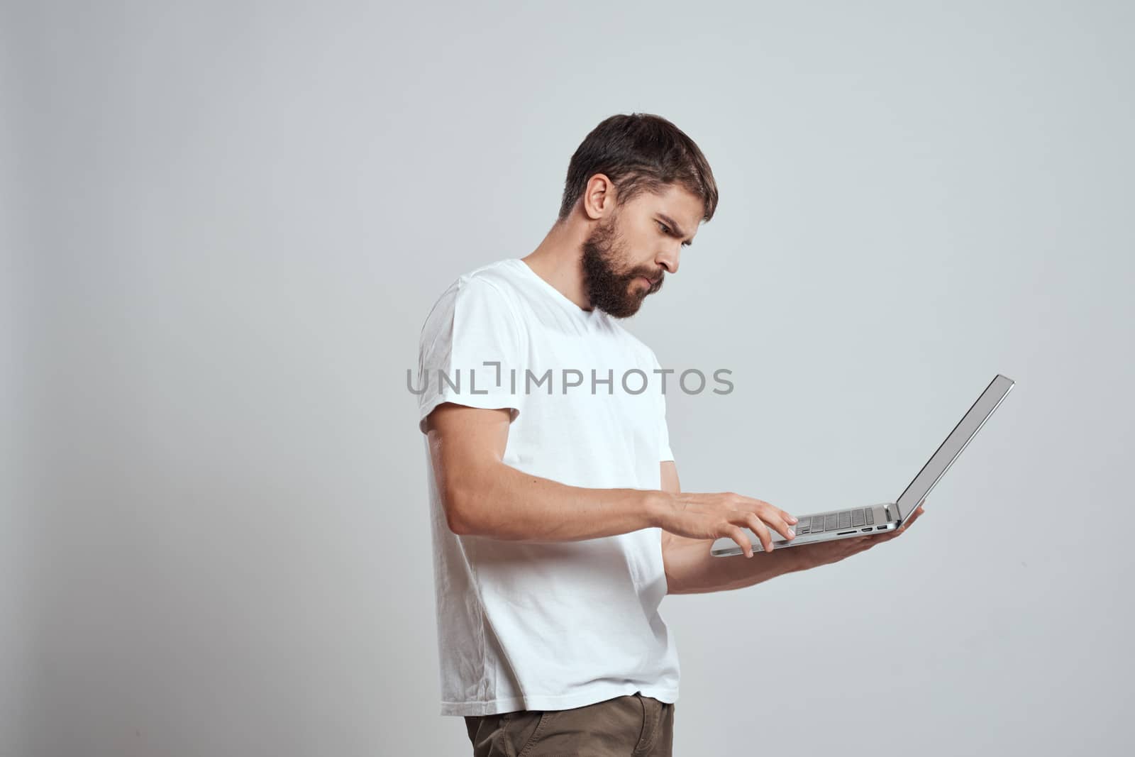 A man with a laptop in his hands on a light background in a white t-shirt emotions light background new technologies by SHOTPRIME