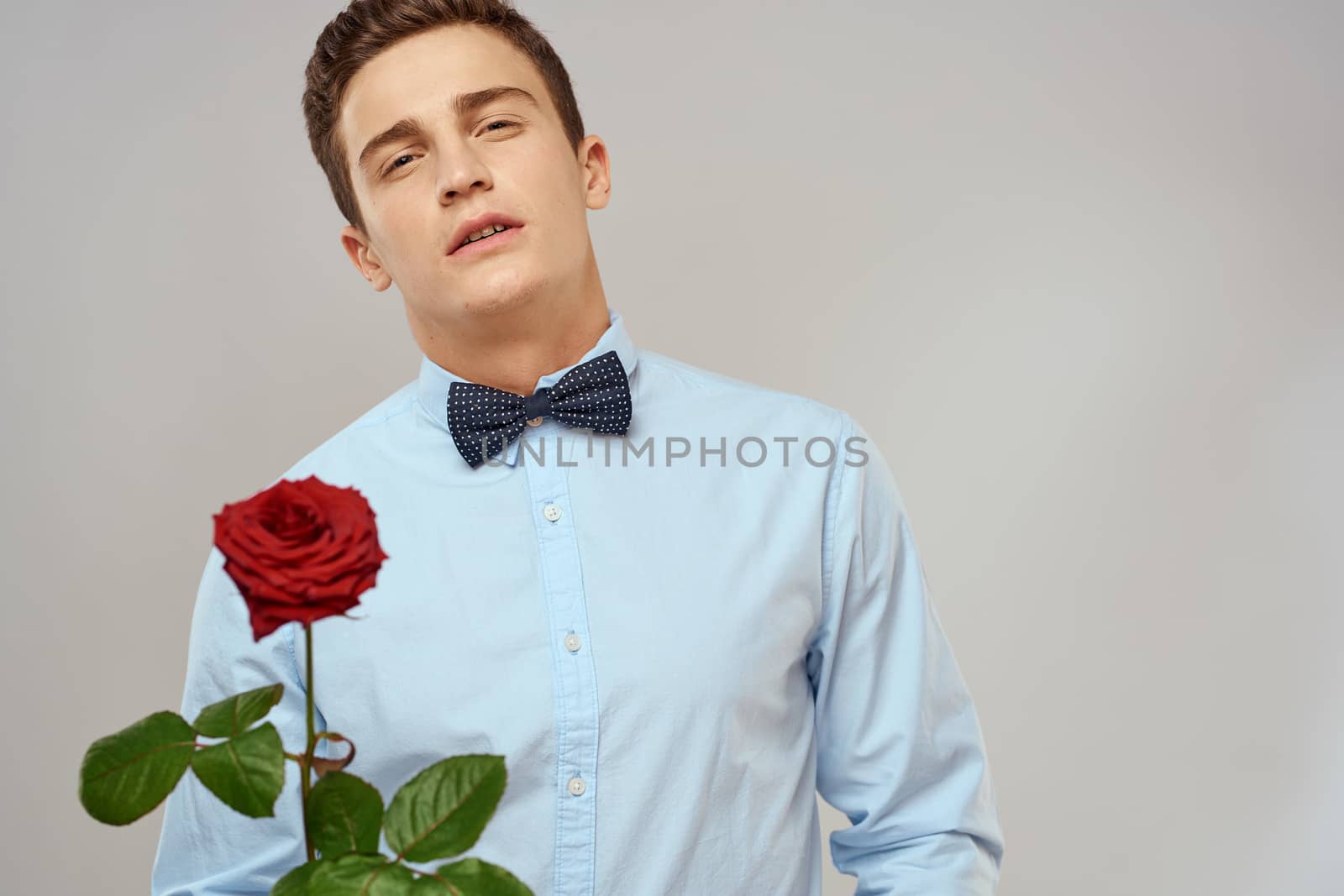 Handsome man with red rose blue shirt bow tie light background cropped view. High quality photo