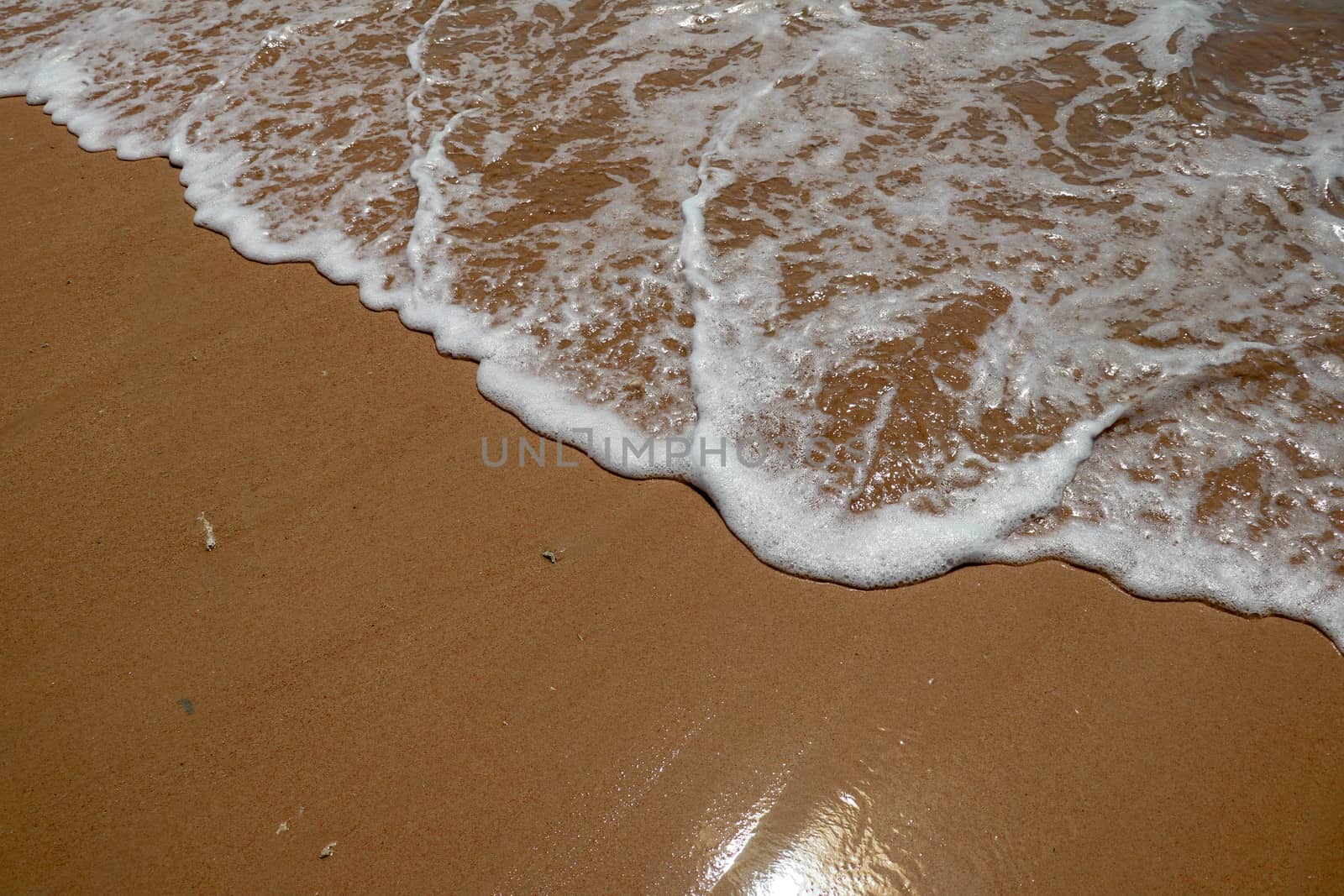 Soft wave of the sea on the sandy beach. Small wave of water on clear sandy beach.