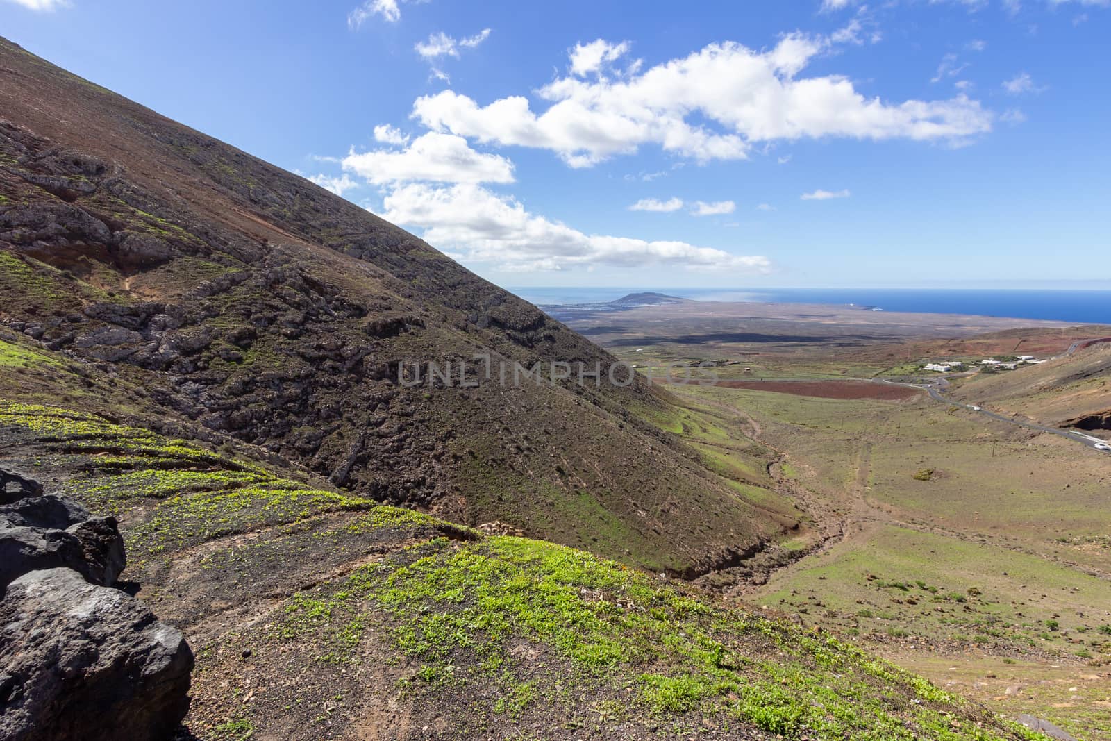 Panoramic view at landscape in the south of canary island Lanzarote nearby Playa Blanca with lava rocks and mountain in the foreground and the atlantic ocean in the background.  The sky is blue with white clouds