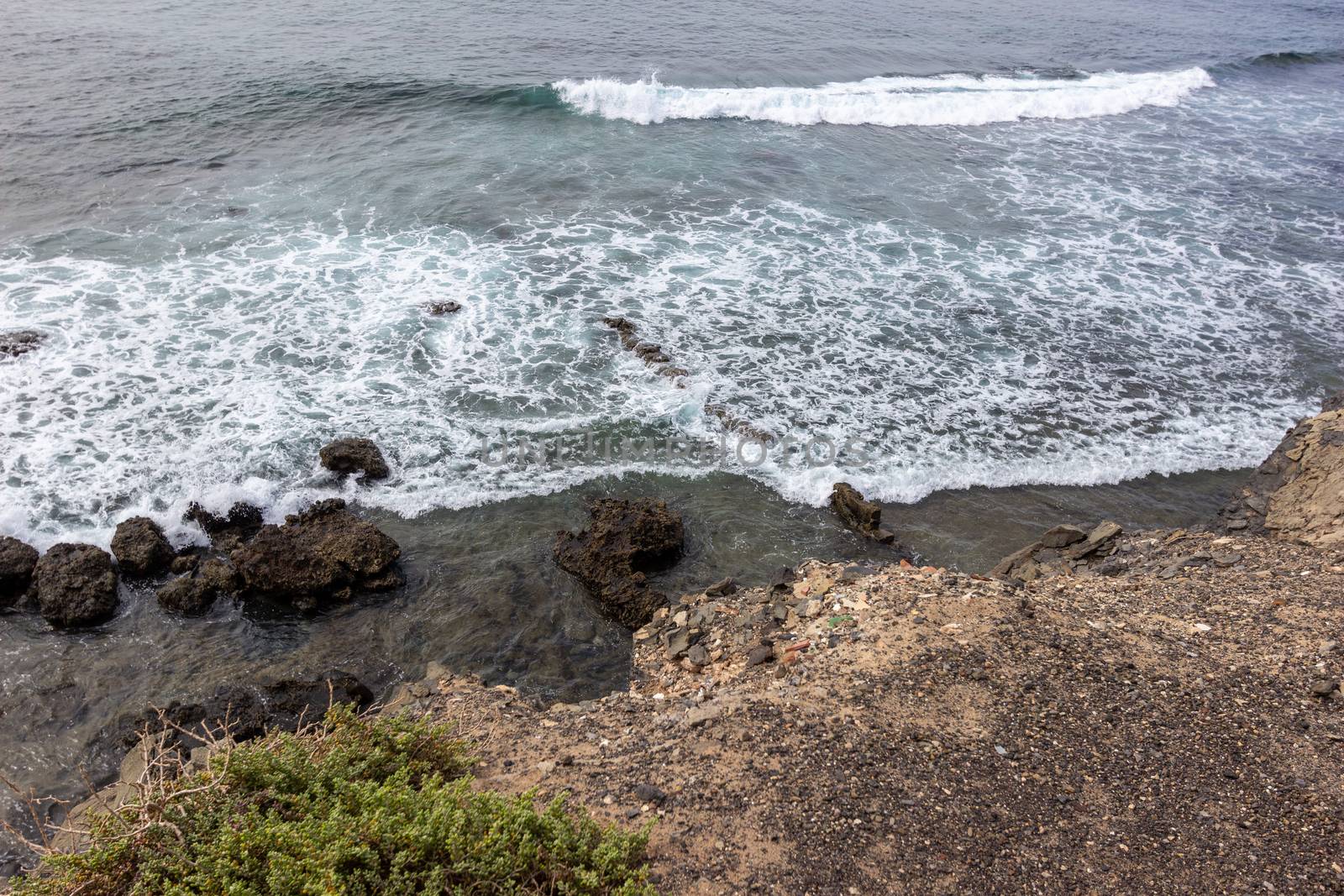 Scenic view at the coastline in the natural park of Jandia (Parque Natural De Jandina) on canary island Fuerteventura, Spain with gravel, lava rocks and rough sea with waves