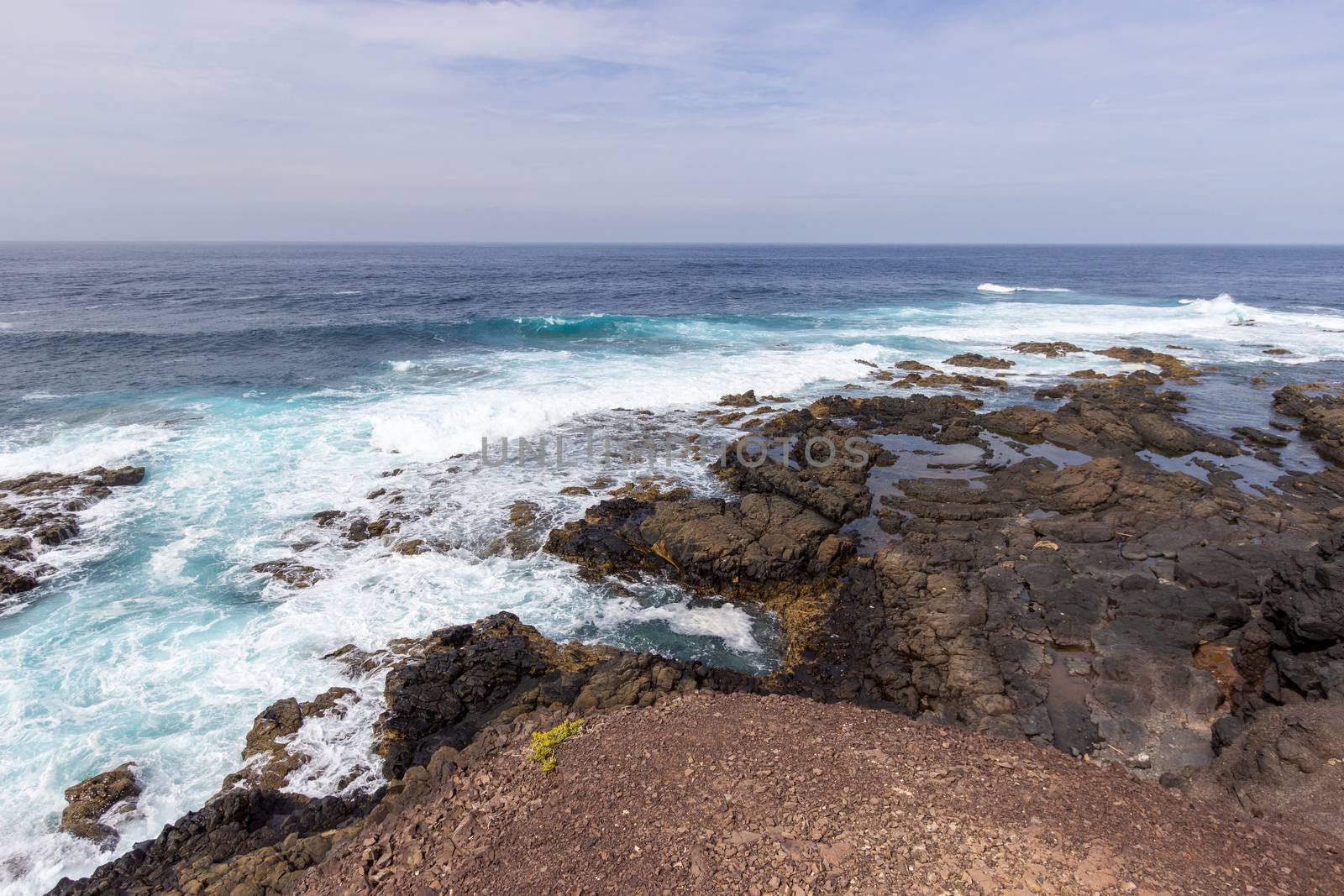 Scenic view at the coastline in the natural park of Jandia (Parque Natural De Jandina) on canary island Fuerteventura, Spain with gravel, lava rocks and rough sea with waves