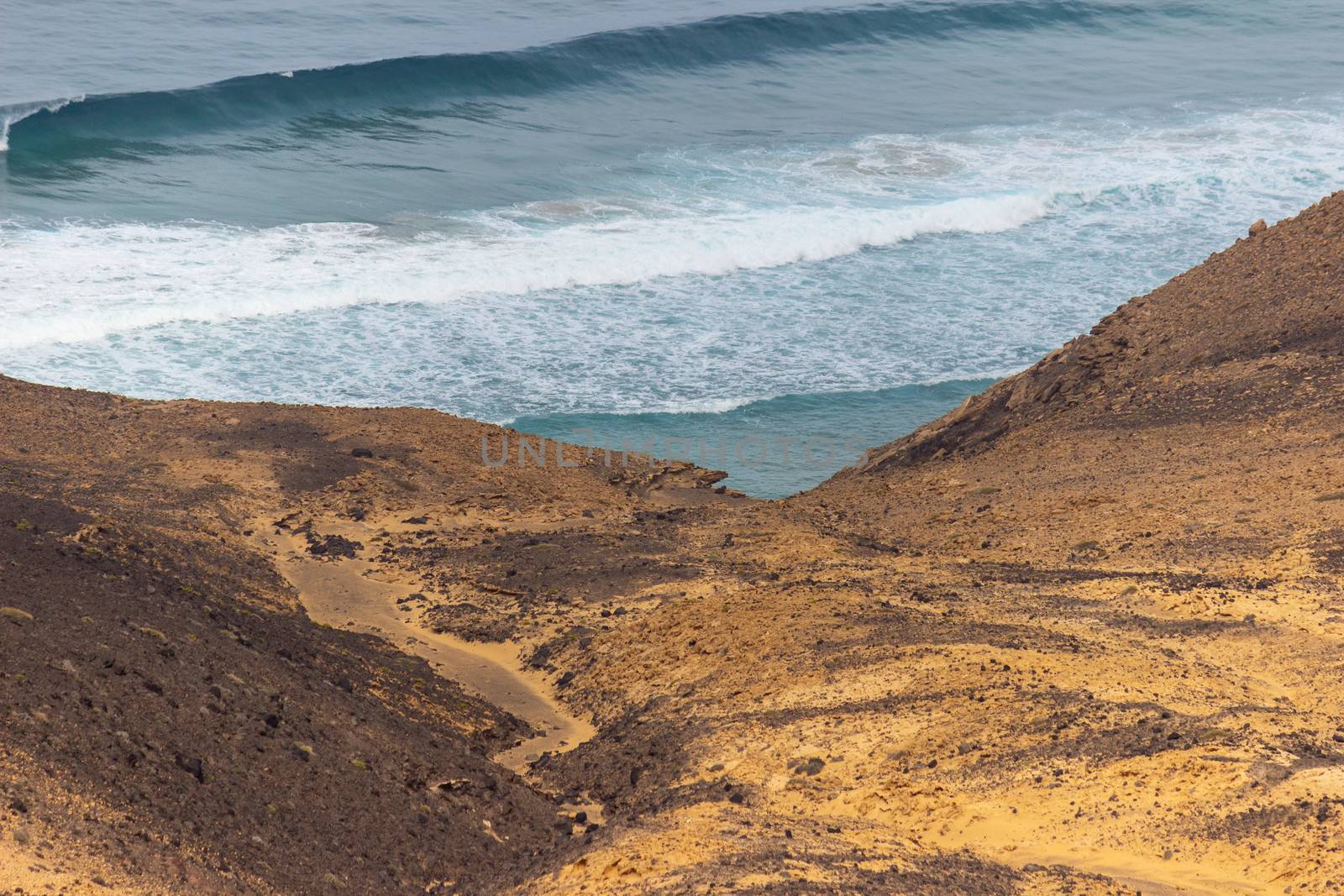 Panoramic view at the coastline in the natural park of Jandia (Parque Natural De Jandina) on canary island Fuerteventura, Spain with gravel, lava rocks and rough sea with waves and mountain range in the background