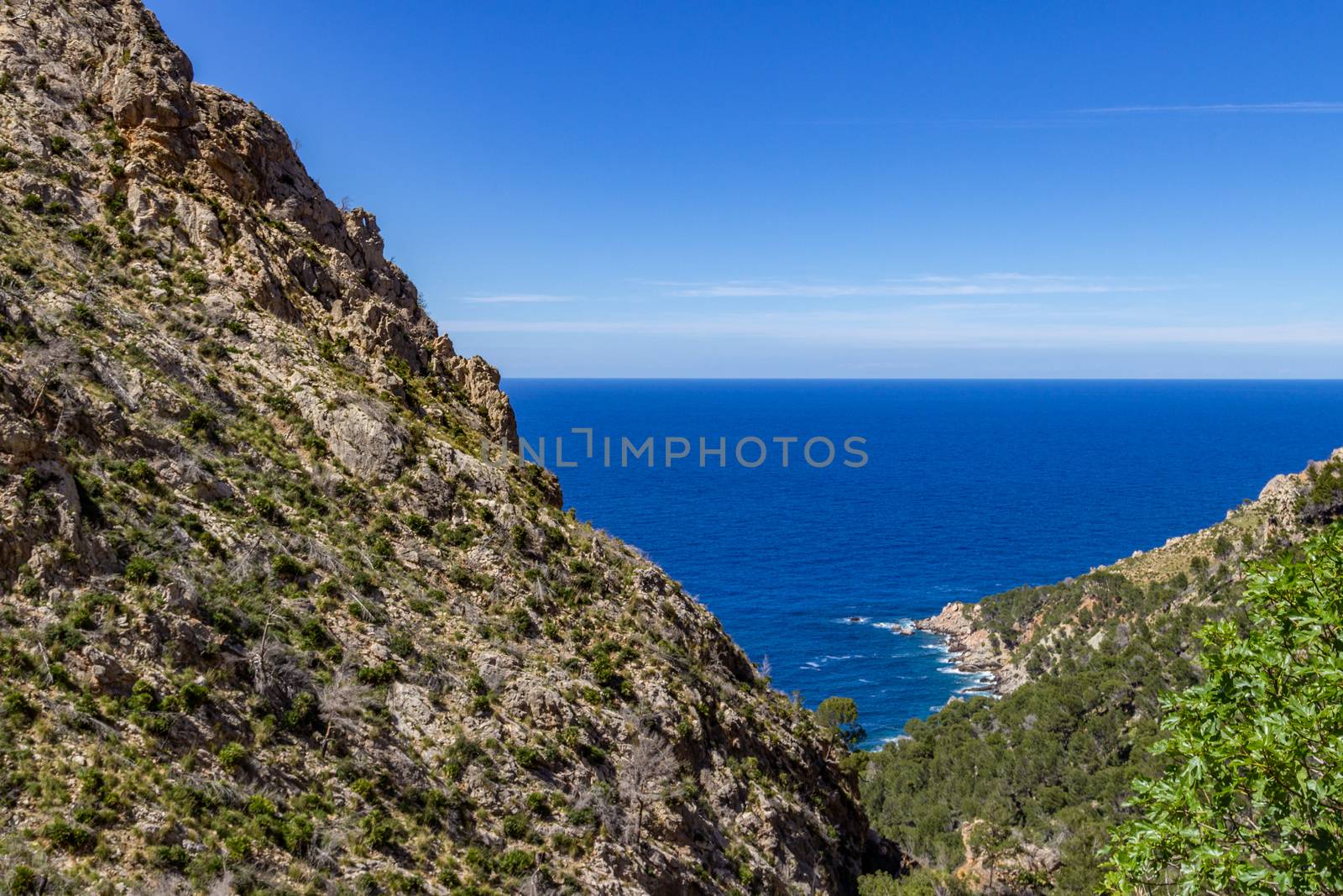 Scenic view in summer at the north coast of Mallorca with mountain in foreground, blue water and blue sky in background 