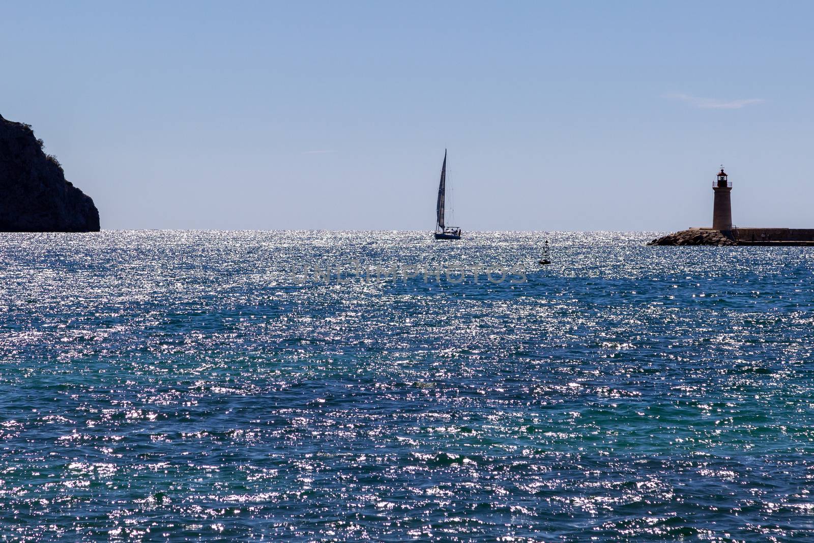 Sailboat in the harbor entrance of Port d' Andratx, Mallorca between a Lighthouse and a mountain