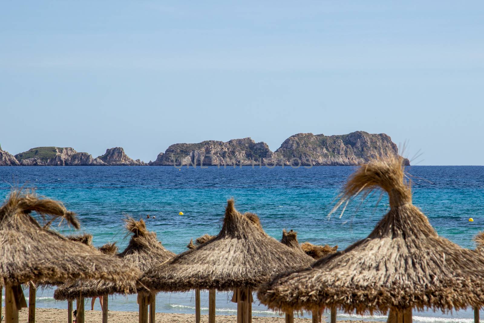 Straw sunshade on the beach,  turquoise water and rocks at S' Arenal, Mallorca