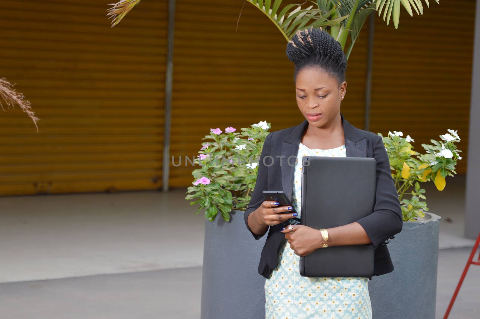 young businesswoman making messages on her cell phone and holds a laptop in her left hand