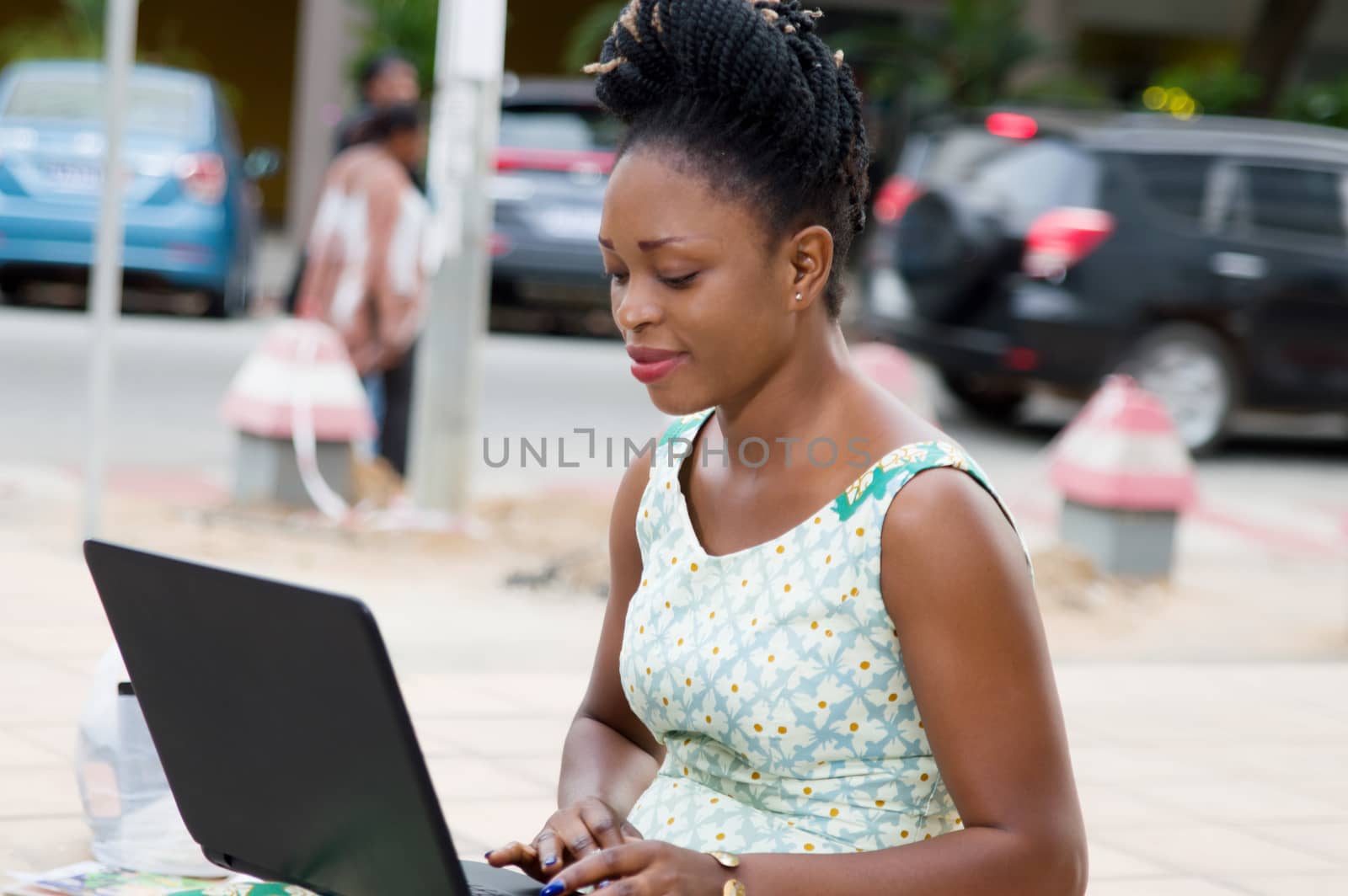 young businesswoman sitting outside working on laptop resting on her lap.