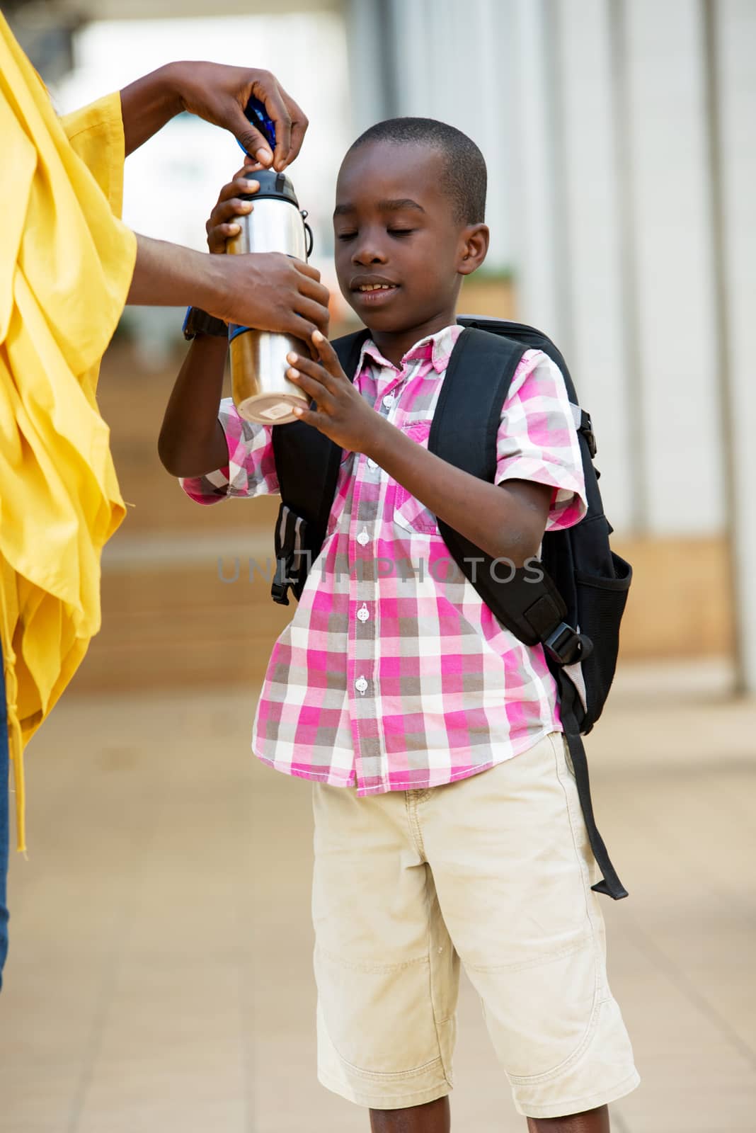 Happy little boy takes his bottle of water in his mother's hand in the morning.