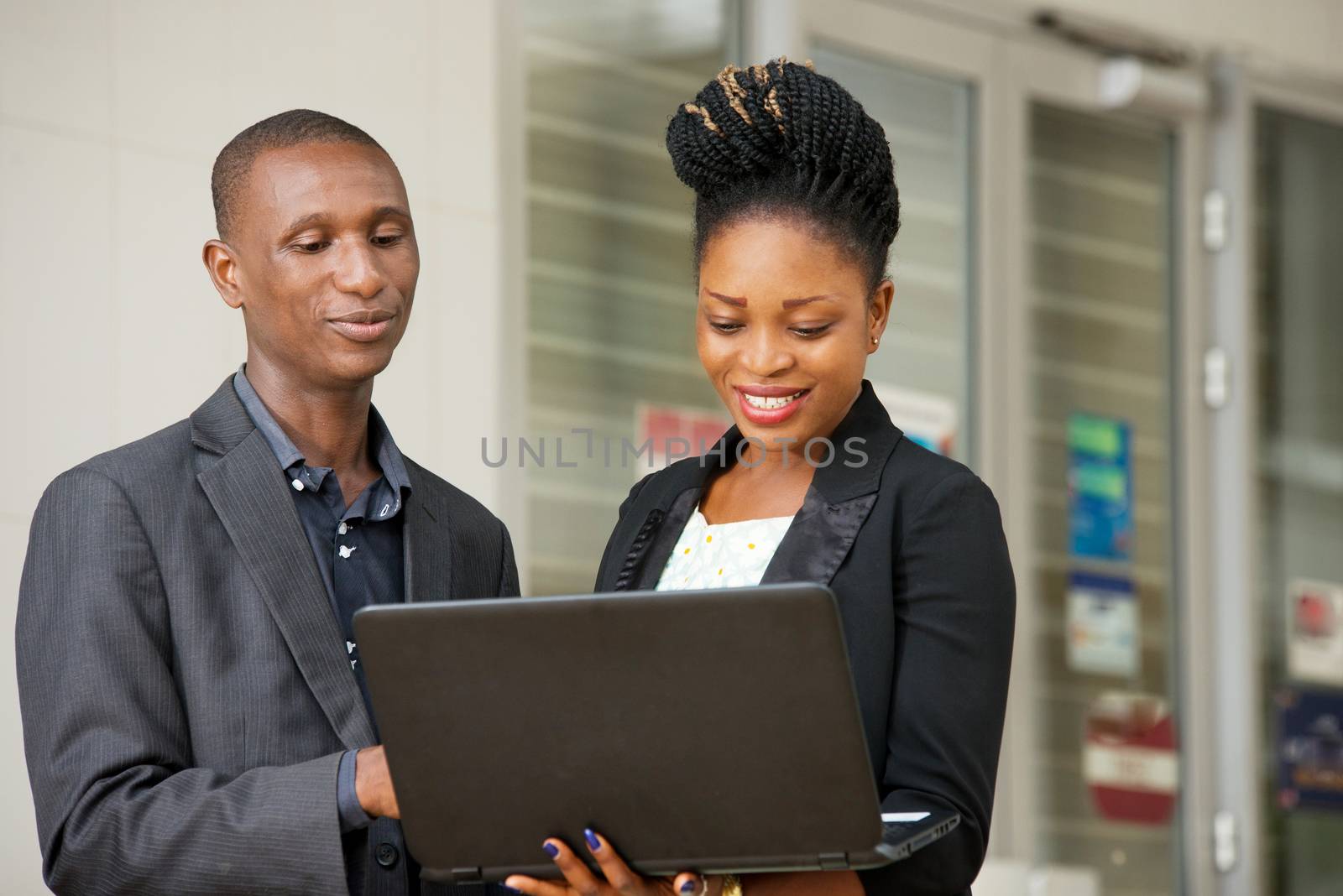 young couple of happy business people standing sharing a laptop in hands
