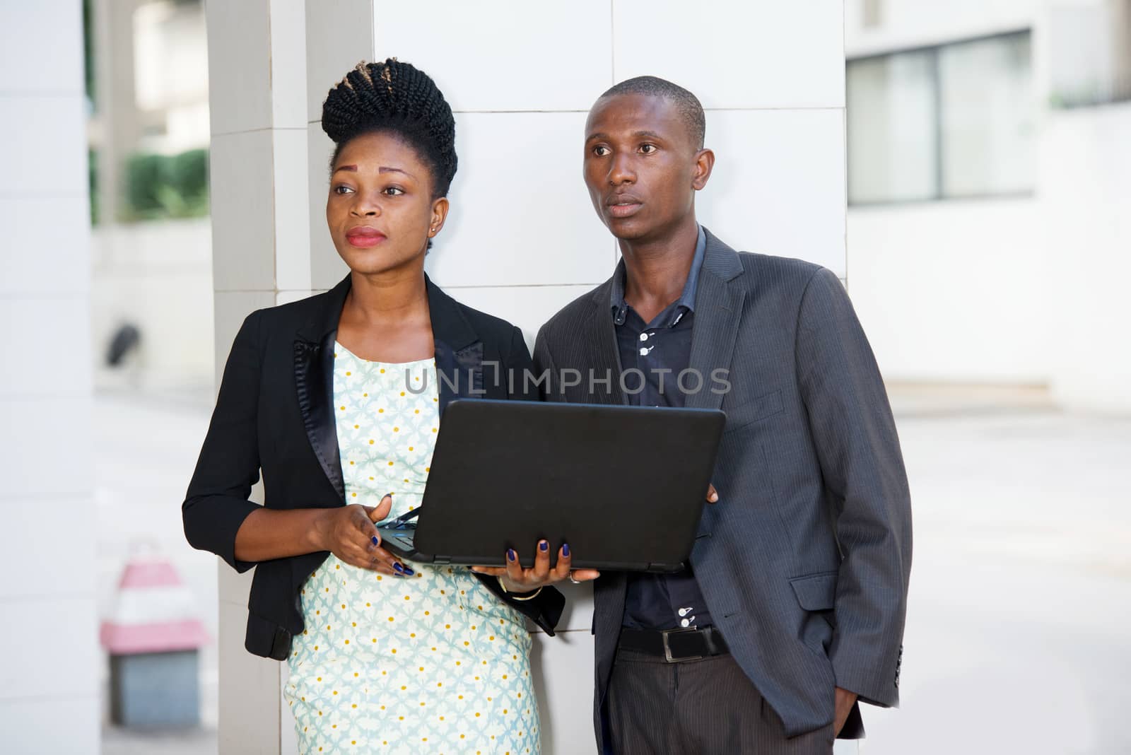 portrait of a businessman and a businesswoman standing near a pillar of a business center and working with a laptop.