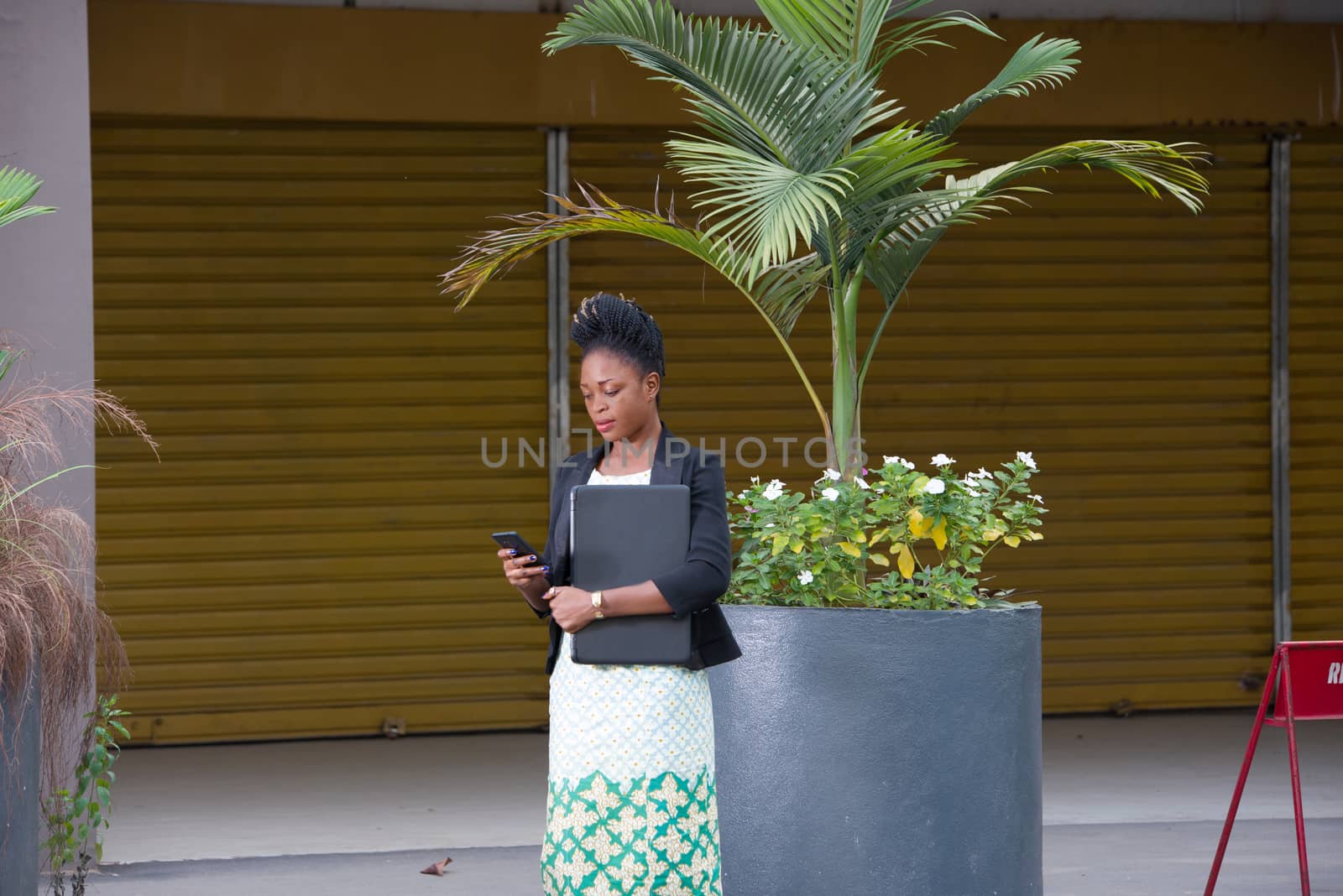 young businesswoman standing with a laptop, reading messages in her mobile phone.