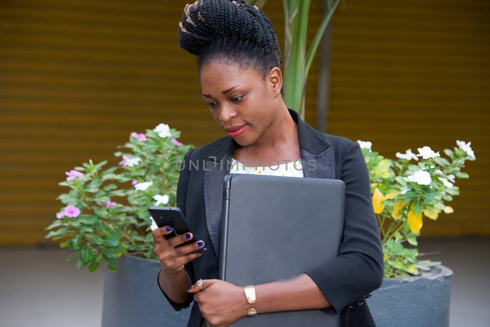 young businesswoman looking at her mobile phone and holding a laptop.