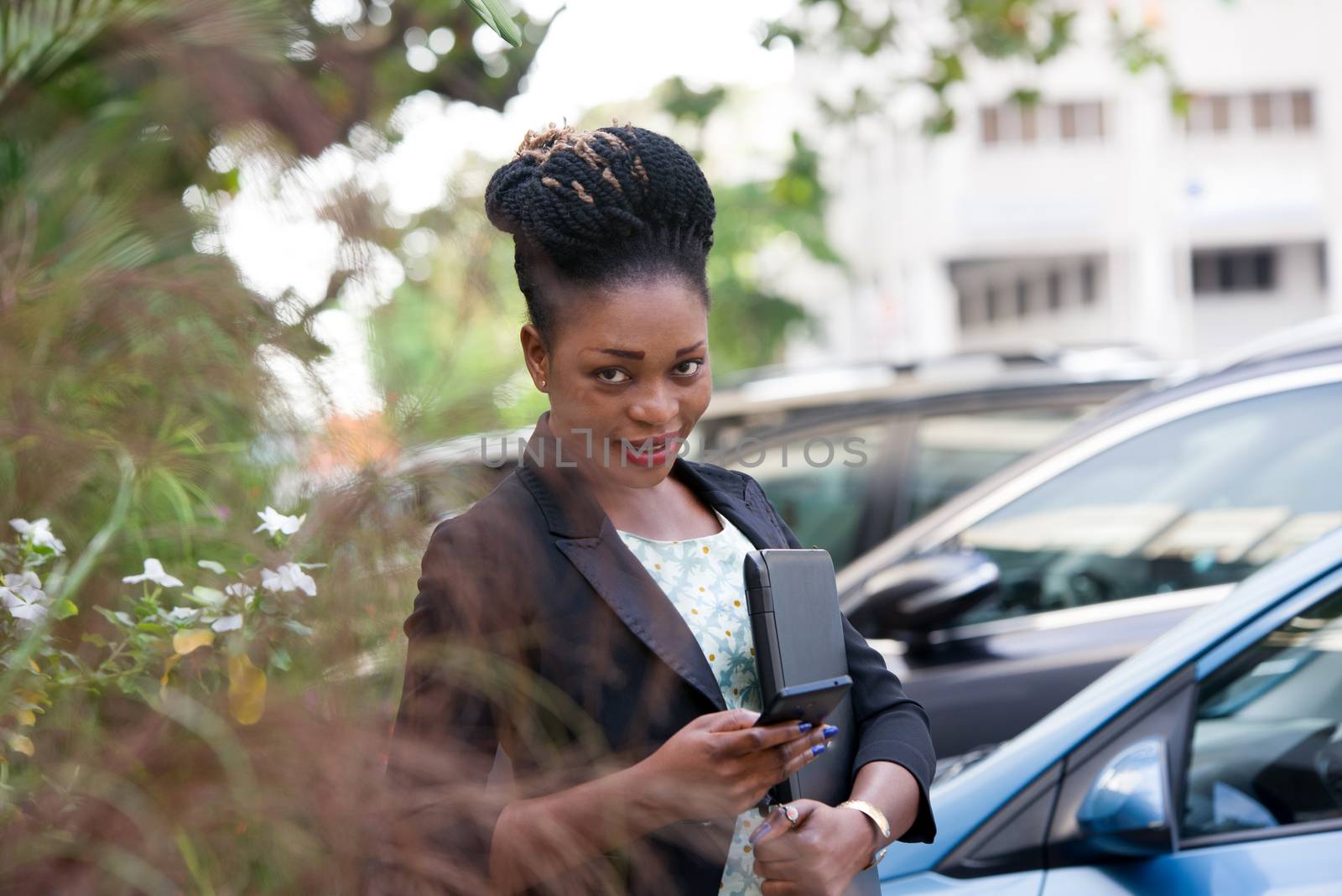 young businesswoman standing behind the flowers is handling her mobile phone.