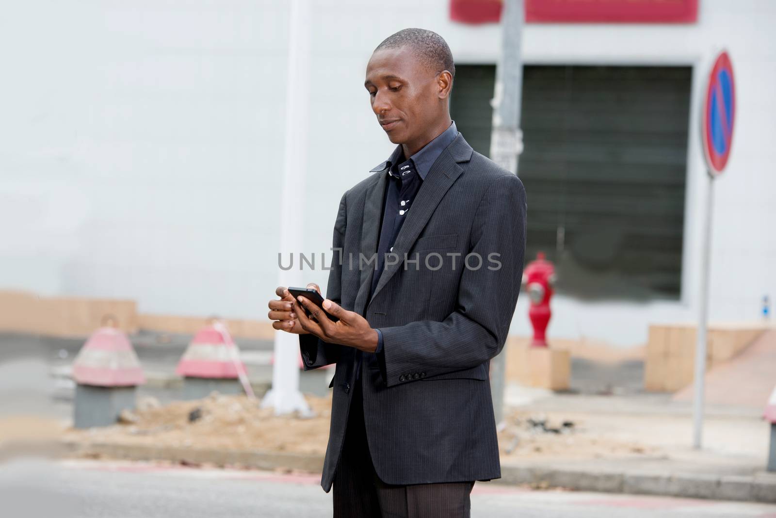 professional businessman in suit standing alone in town and manipulating his mobile phone outdoors