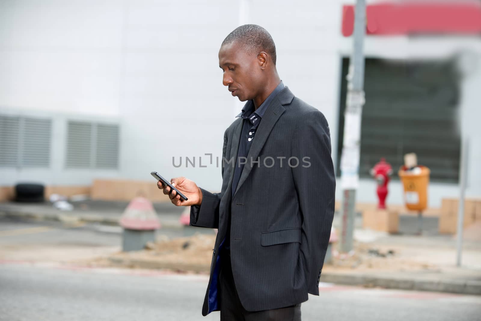 Image of a businessman in a suit standing on the street and checking his mobile phone