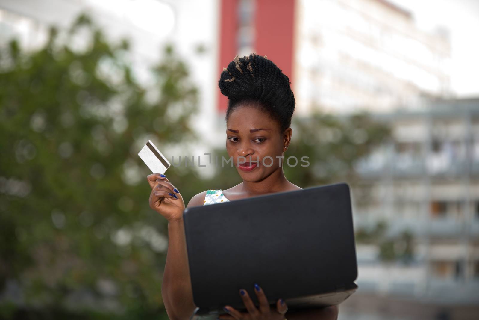 Smiling and confident businesswoman doing online shopping through a laptop and a credit card standing in the street