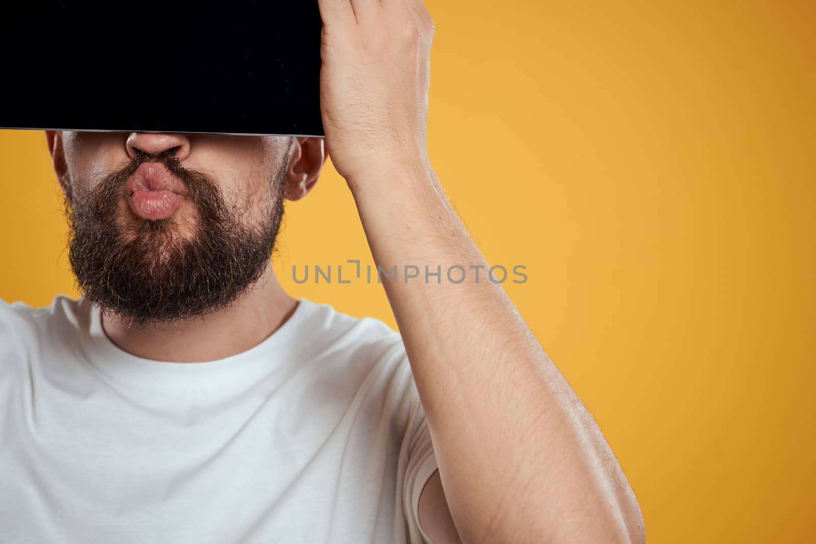Portrait of a man with a tablet in front of his face on a yellow background cropped view of a white T-shirt Copy Space. High quality photo