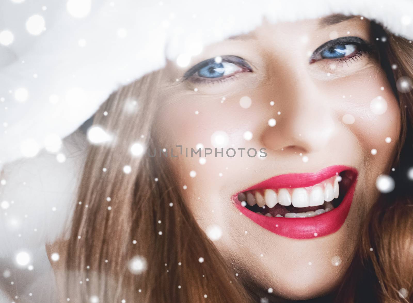 Happy Christmas and winter holiday portrait of young woman in white hooded fur coat, snow on blue background, fashion and lifestyle campaign