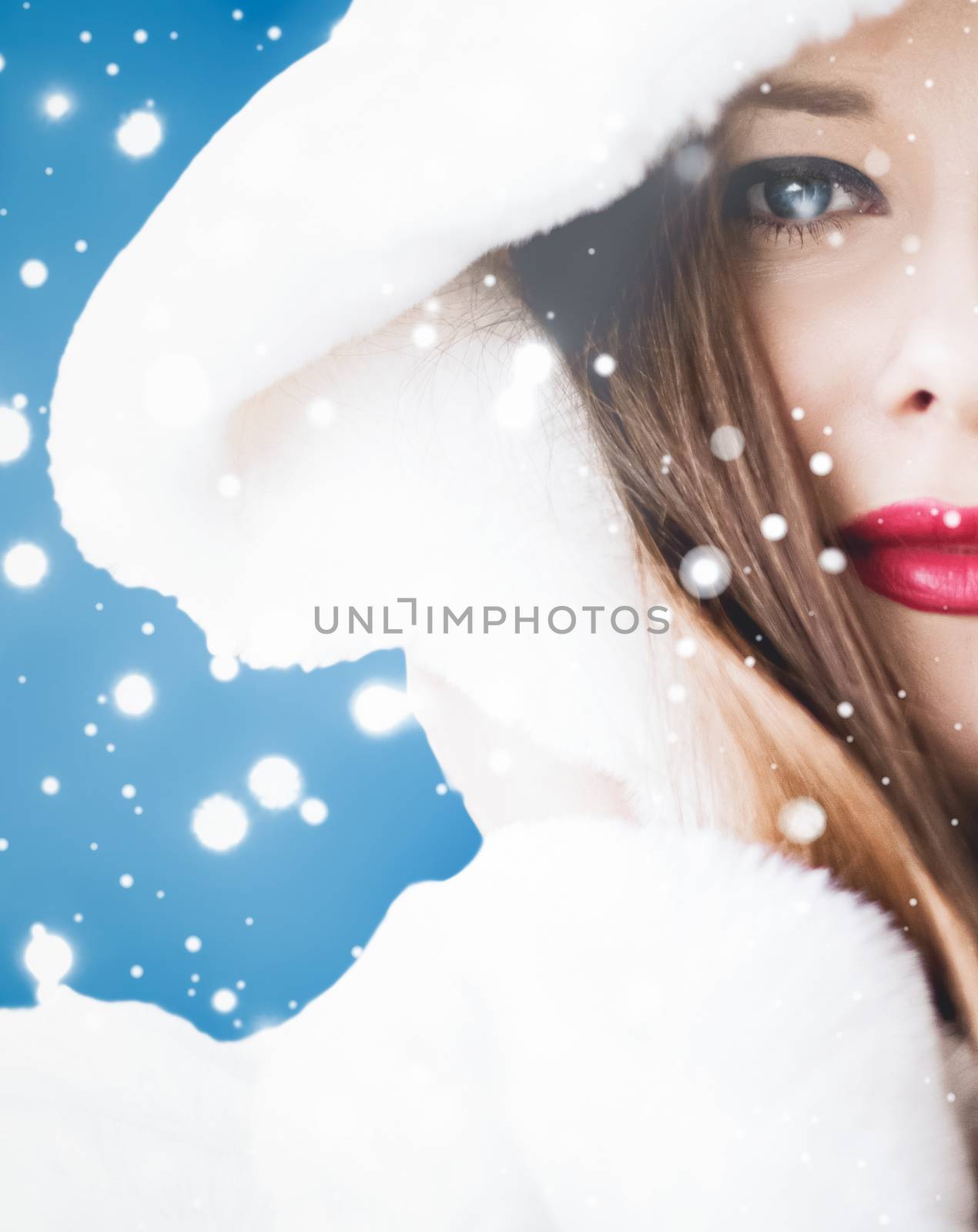 Happy Christmas and winter holiday portrait of young woman in white hooded fur coat, snow on blue background, fashion and lifestyle campaign